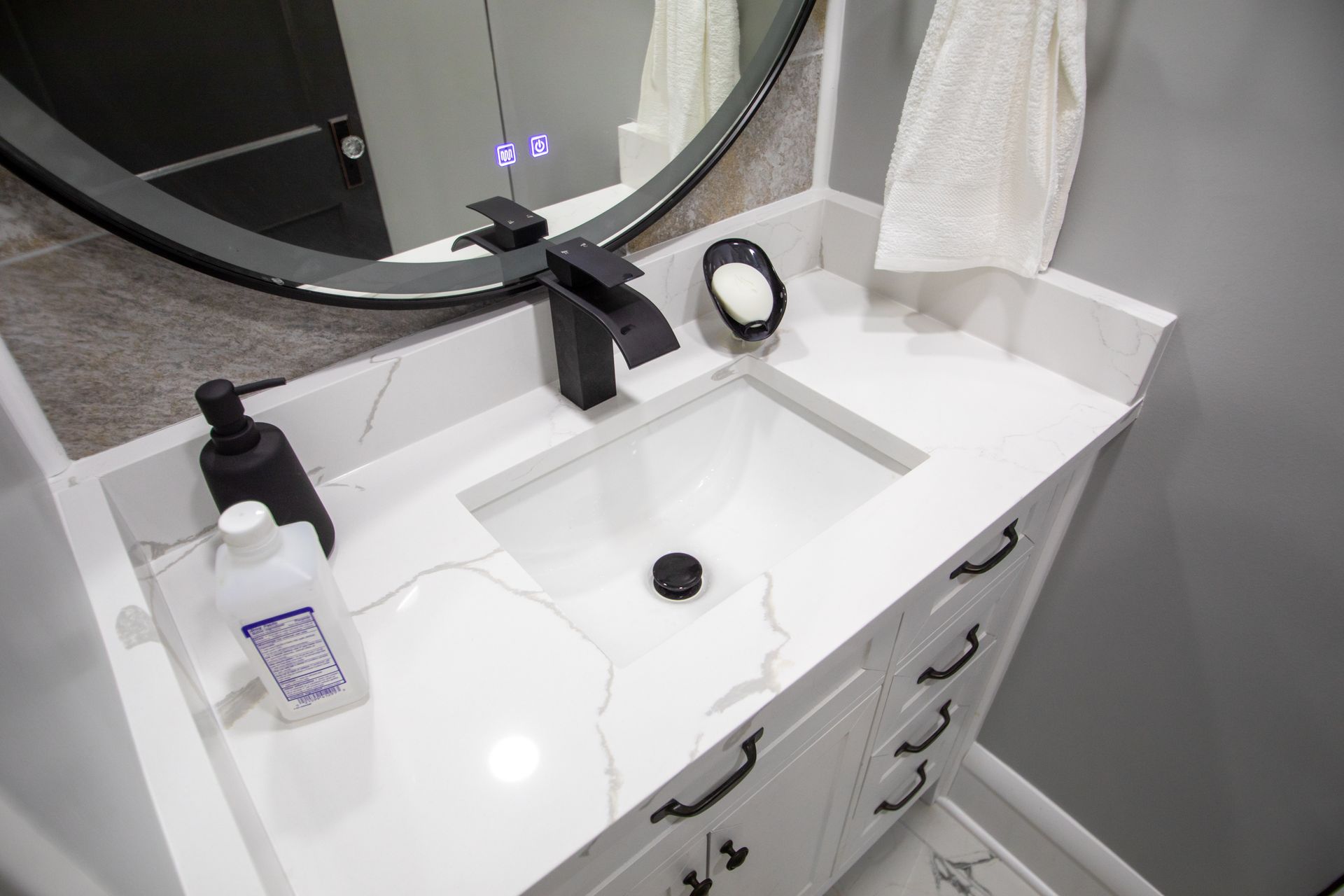 White bathroom vanity with black faucet, round mirror, and soap dispenser.