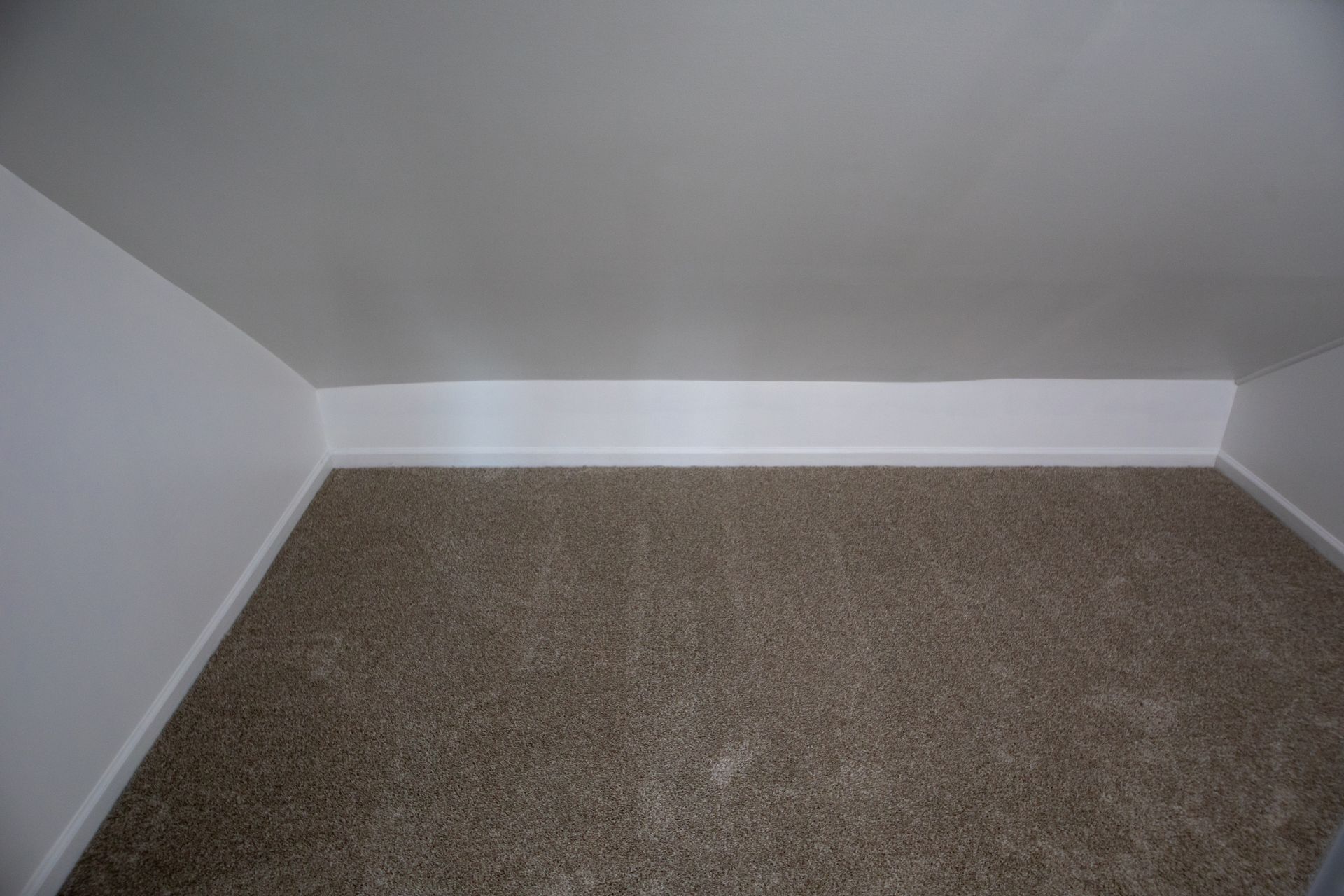 Empty, beige-carpeted room with white walls and a slanted ceiling.