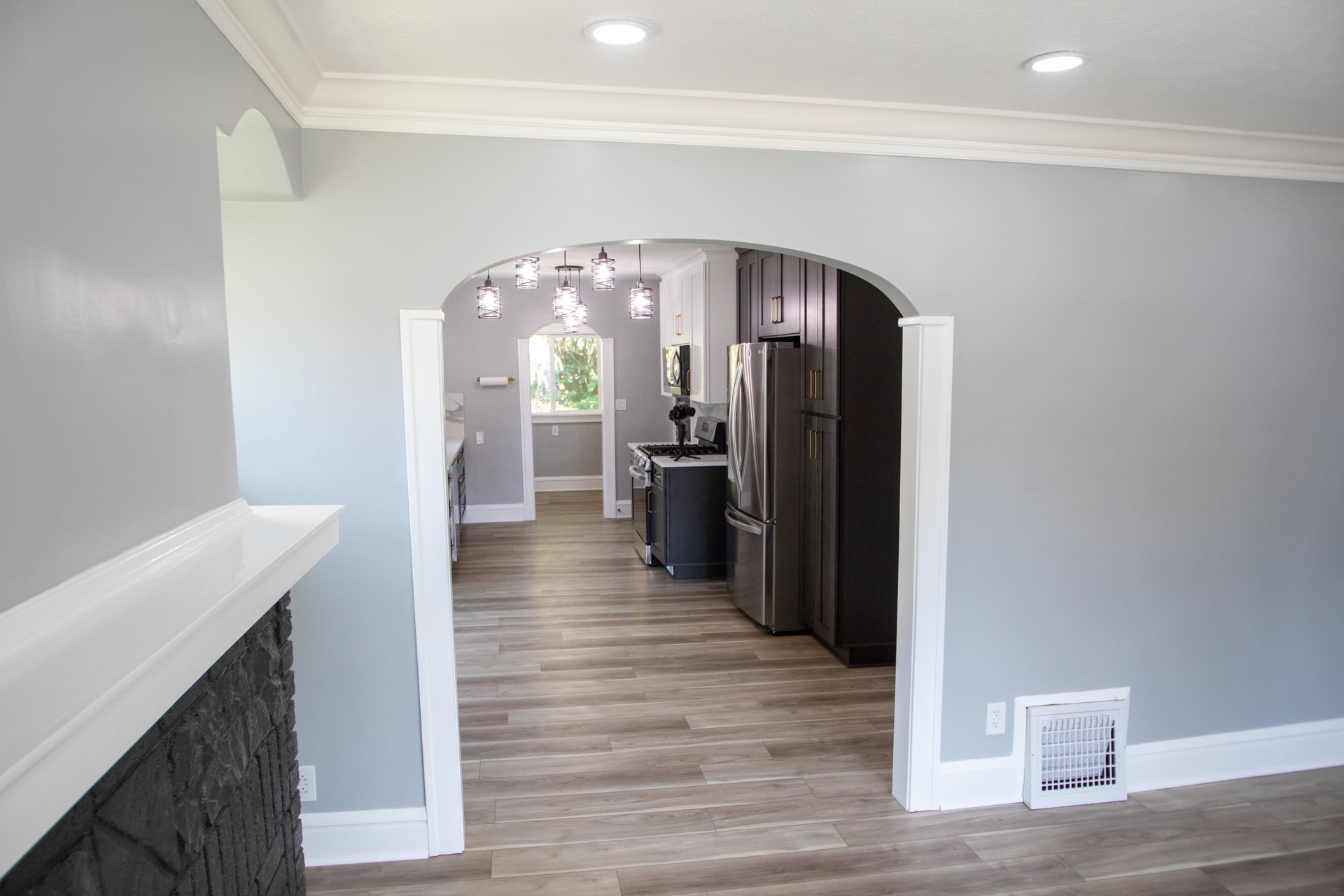 Interior view: living room with arched doorway leading to a kitchen with gray walls, light wood floors.