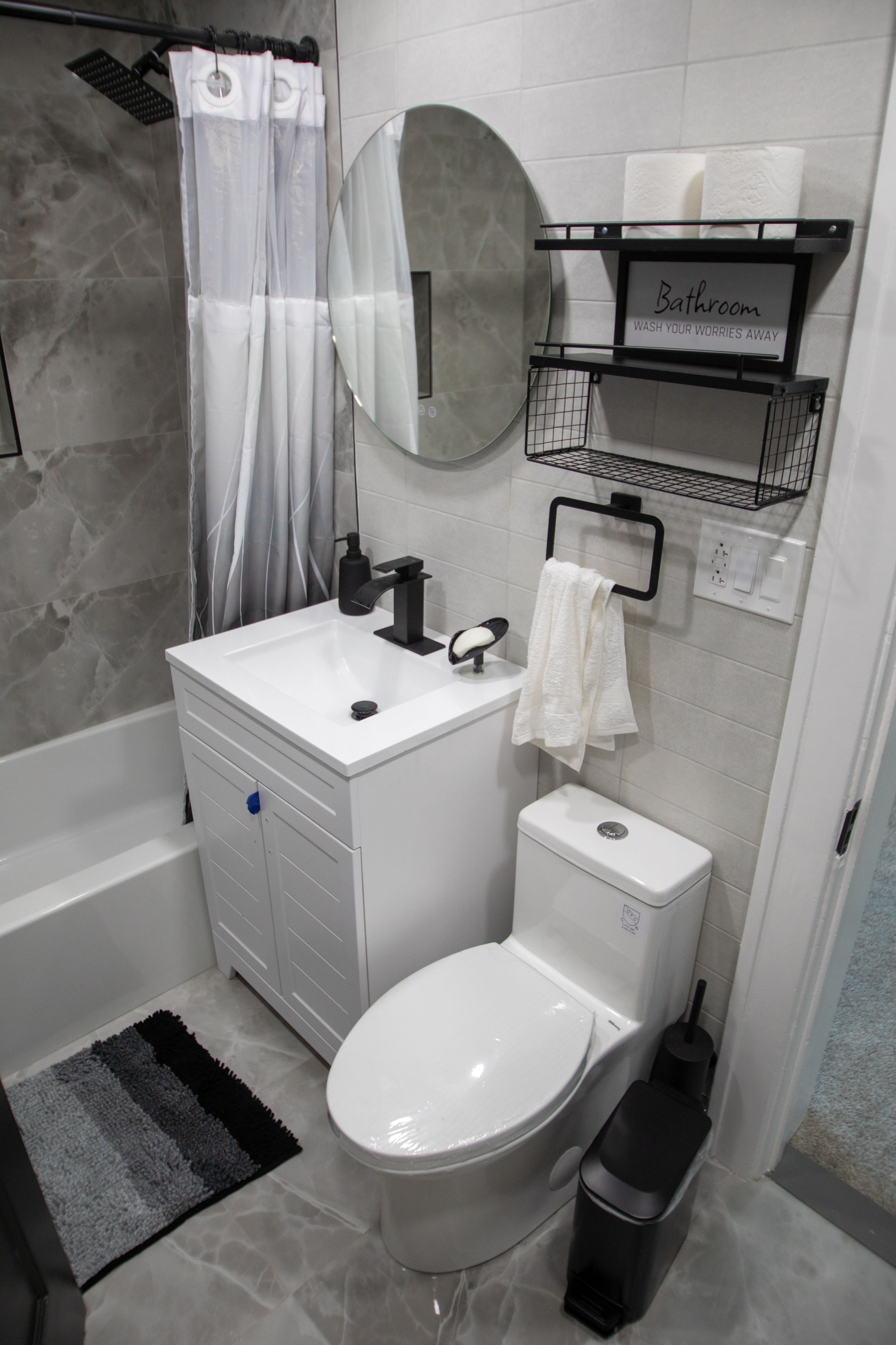 Small modern bathroom with a white vanity, toilet, and gray tiled walls.