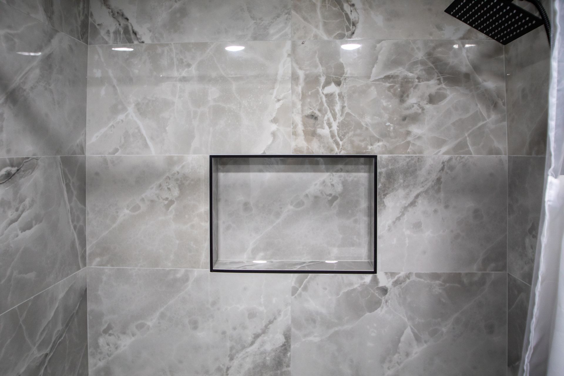 Gray marble tiled shower wall with a recessed black-framed shelf and a black showerhead.