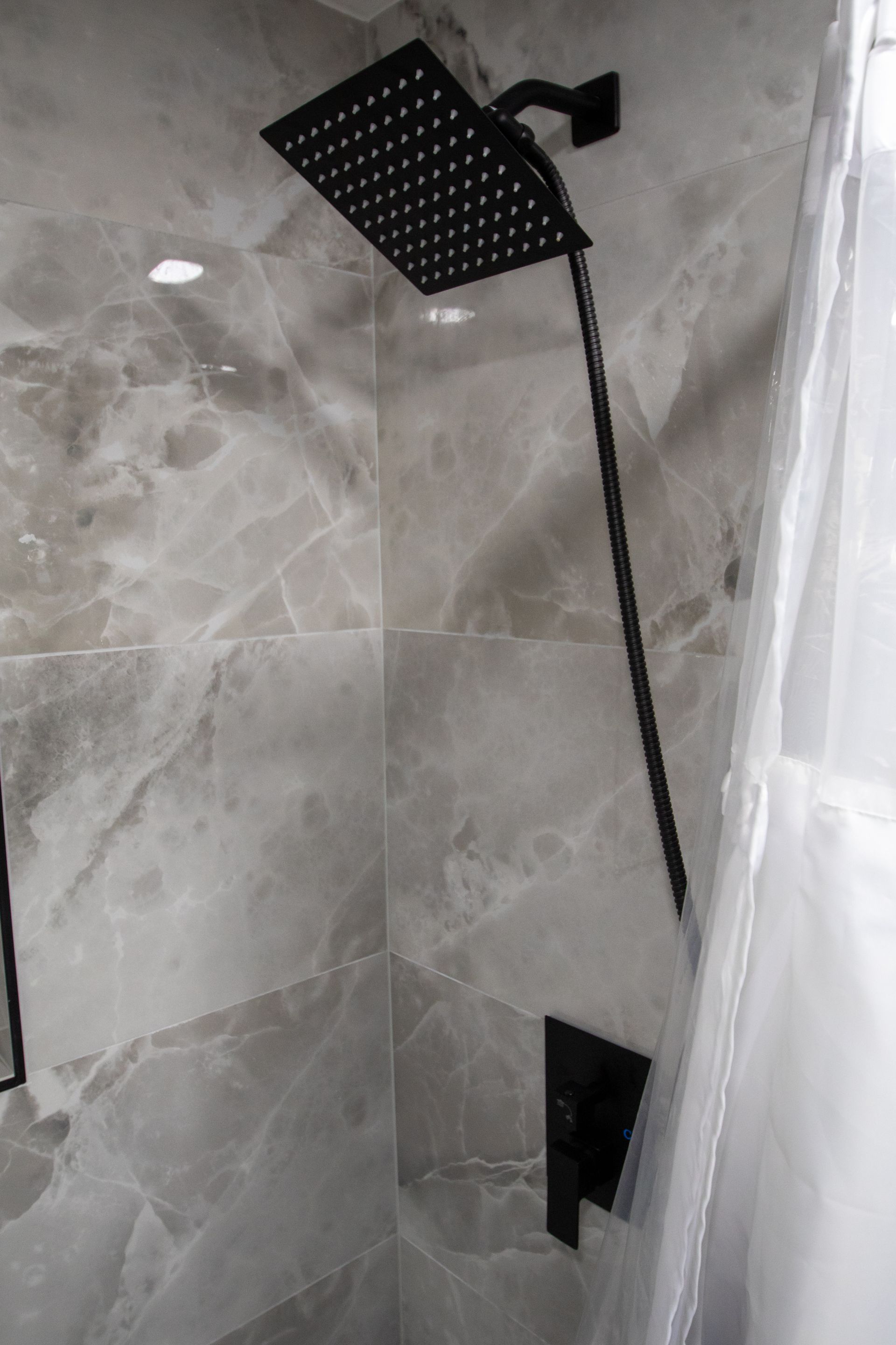 Black showerhead and faucet against a marble tiled shower wall.