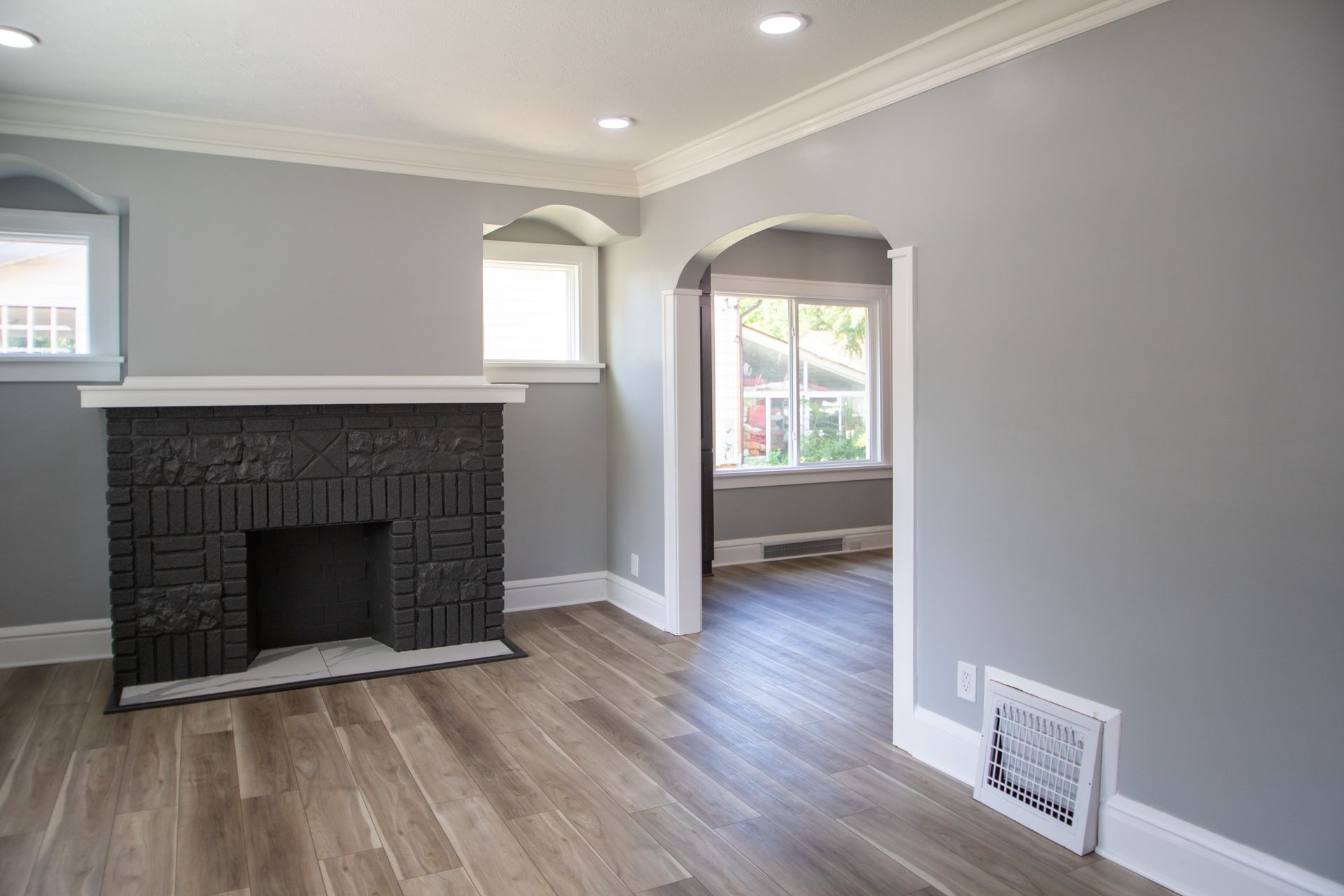 Gray living room with black fireplace, archway, and wood flooring.