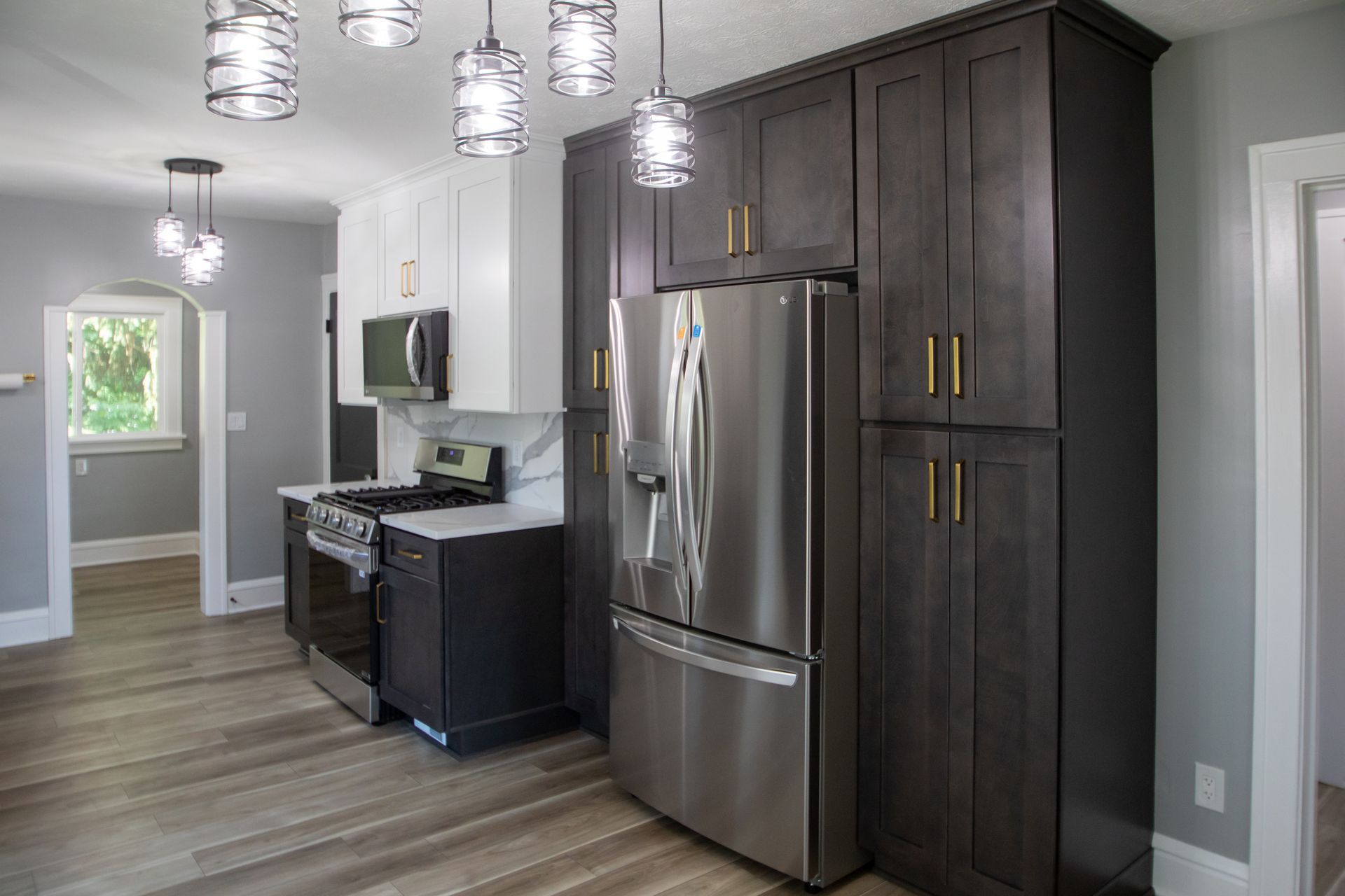 Modern kitchen with gray cabinets, stainless steel refrigerator, and pendant lights.