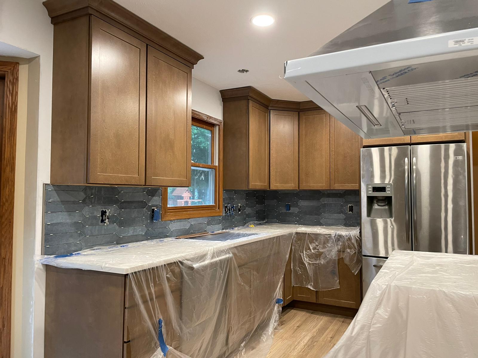 Kitchen undergoing renovation, with brown cabinets, stainless steel appliances, and a gray backsplash.