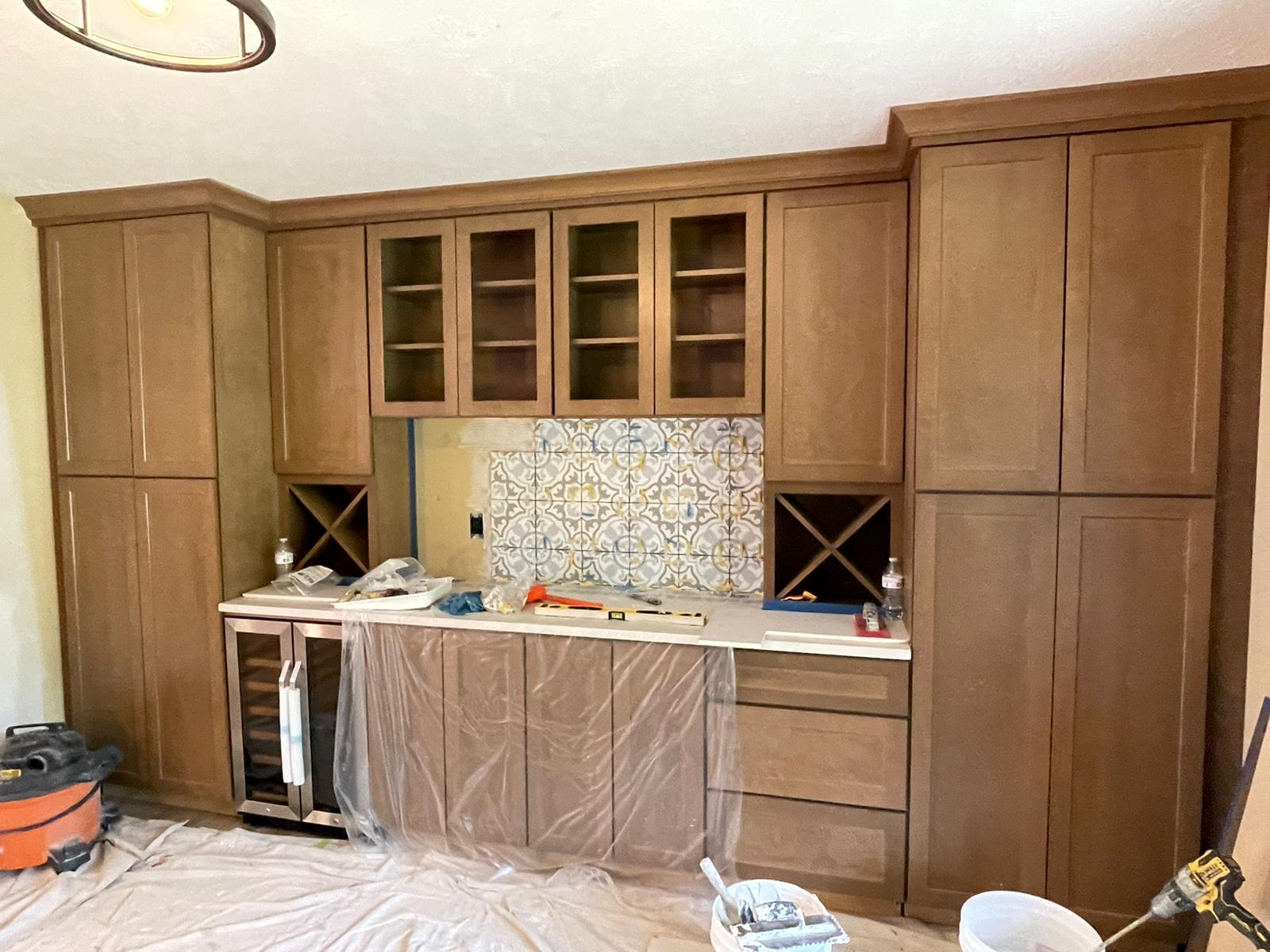 Wooden bar with cabinets, a wine fridge, and tile backsplash, under construction.