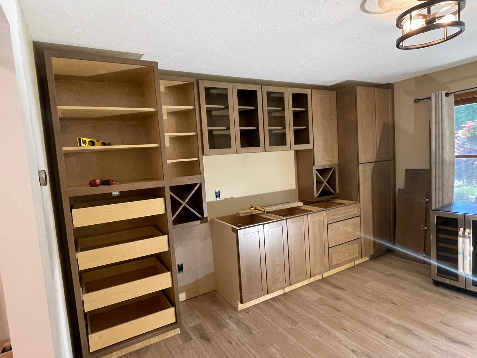 Kitchen cabinetry under construction: unfinished wood cabinets and shelves against a wall.