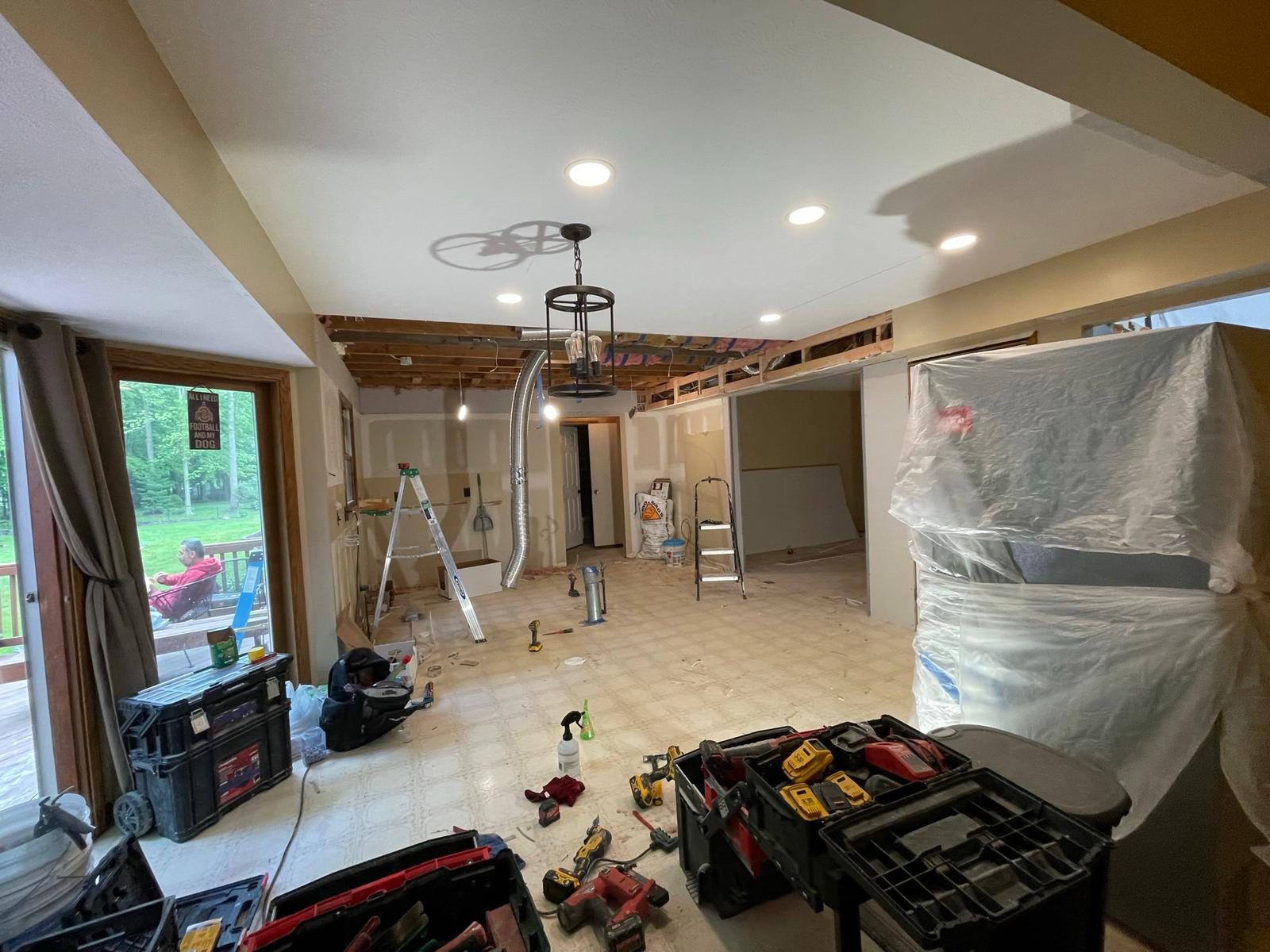 Kitchen remodel in progress, open ceiling, tools and equipment scattered across the floor, and a covered appliance.
