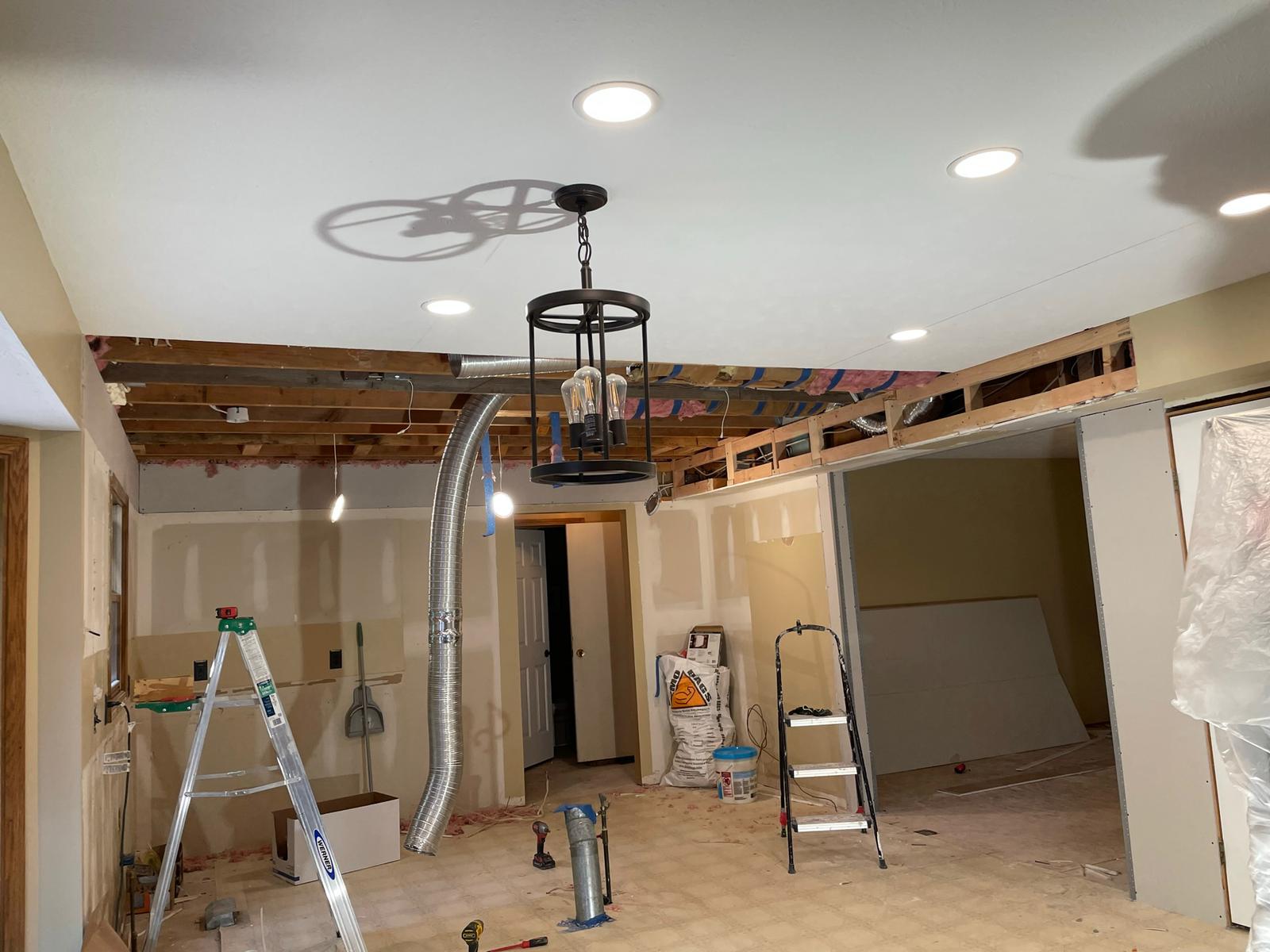Room under renovation with exposed ceiling beams, drywall, and a hanging light fixture.