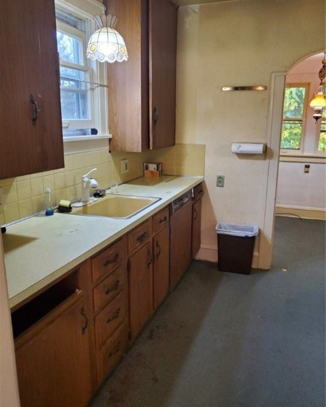 Kitchen with light wood cabinets, off-white countertops, yellow sink, and a view into another room.