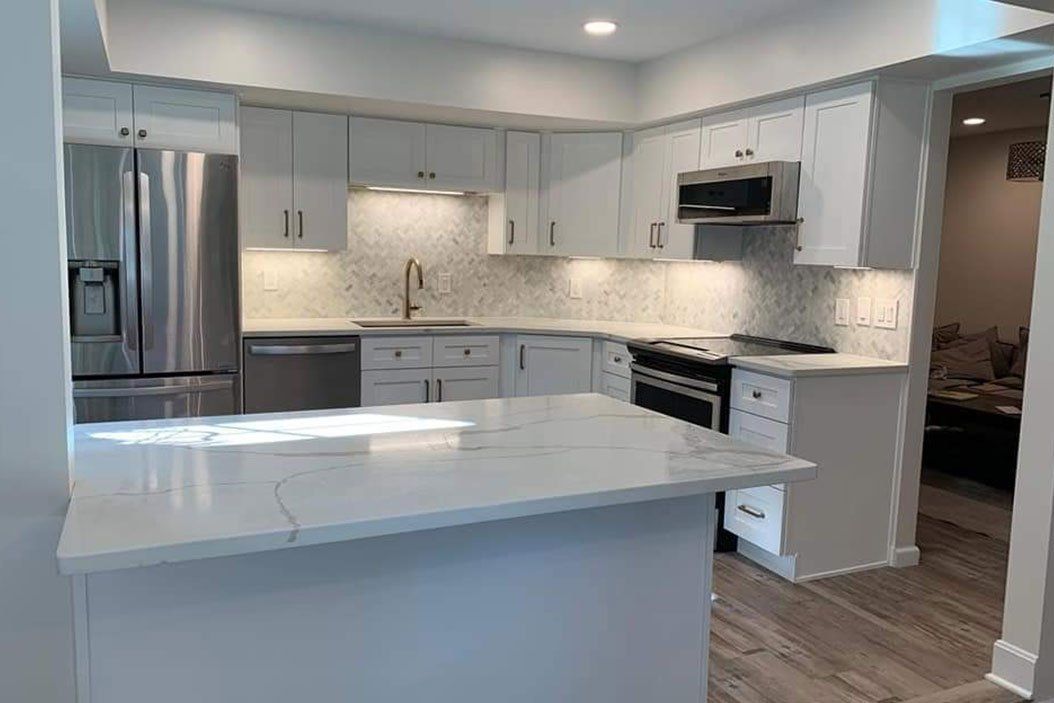 Modern white kitchen with a stainless steel refrigerator, island, and backsplash.
