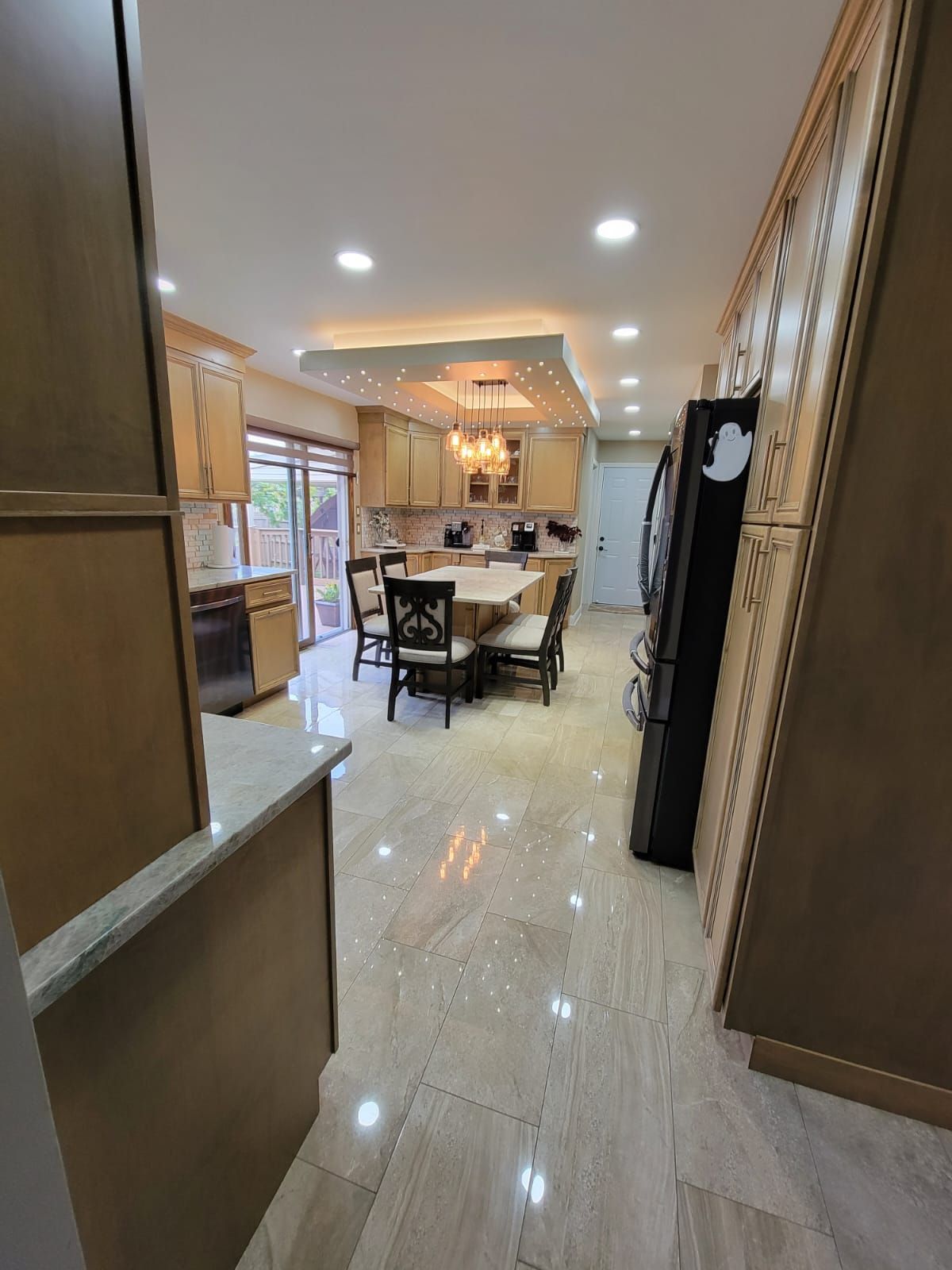 Kitchen interior with light-colored cabinets, tile floor, dining table, and black refrigerator.