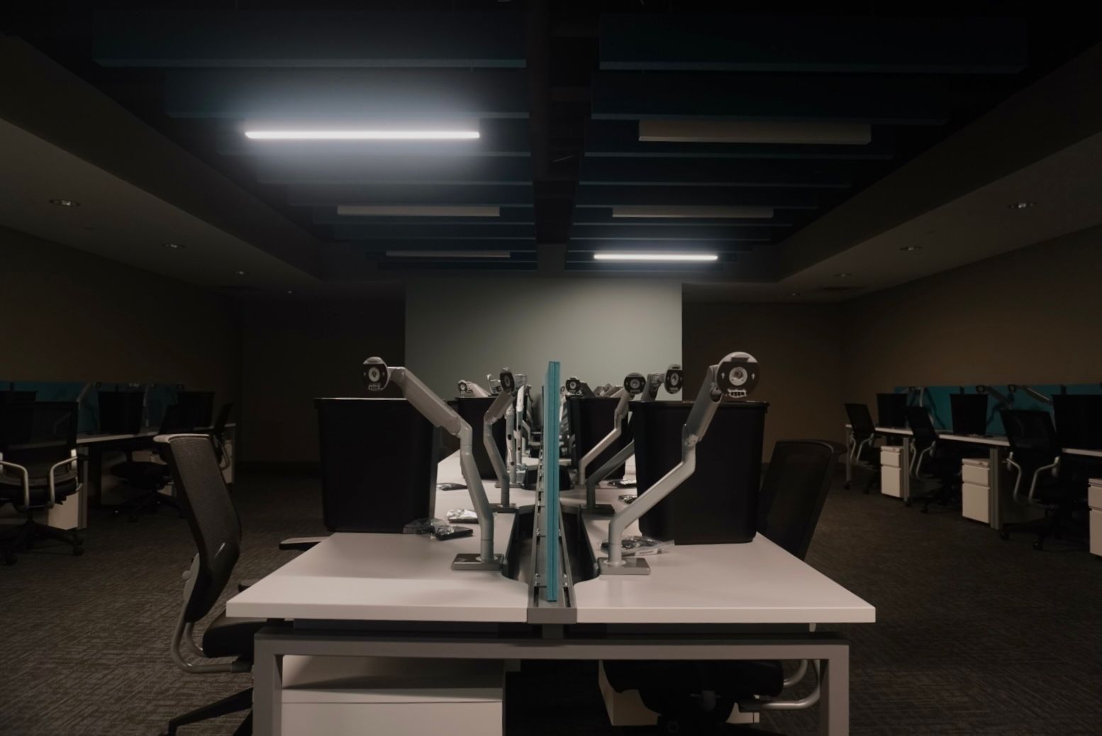 Dark office with rows of empty desks. Overhead lights illuminate the space.
