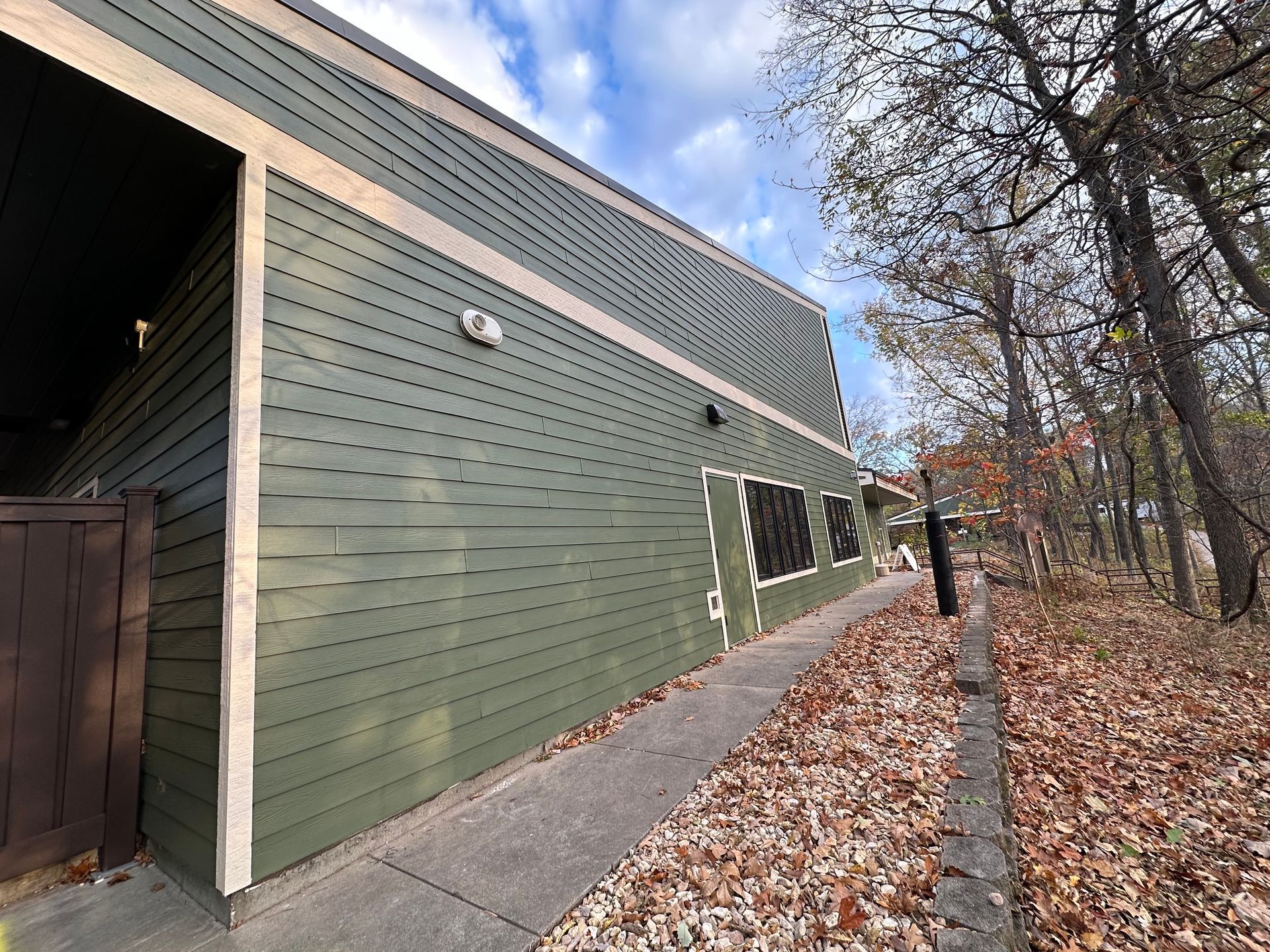 Green building exterior next to trees and a walkway with fallen leaves.