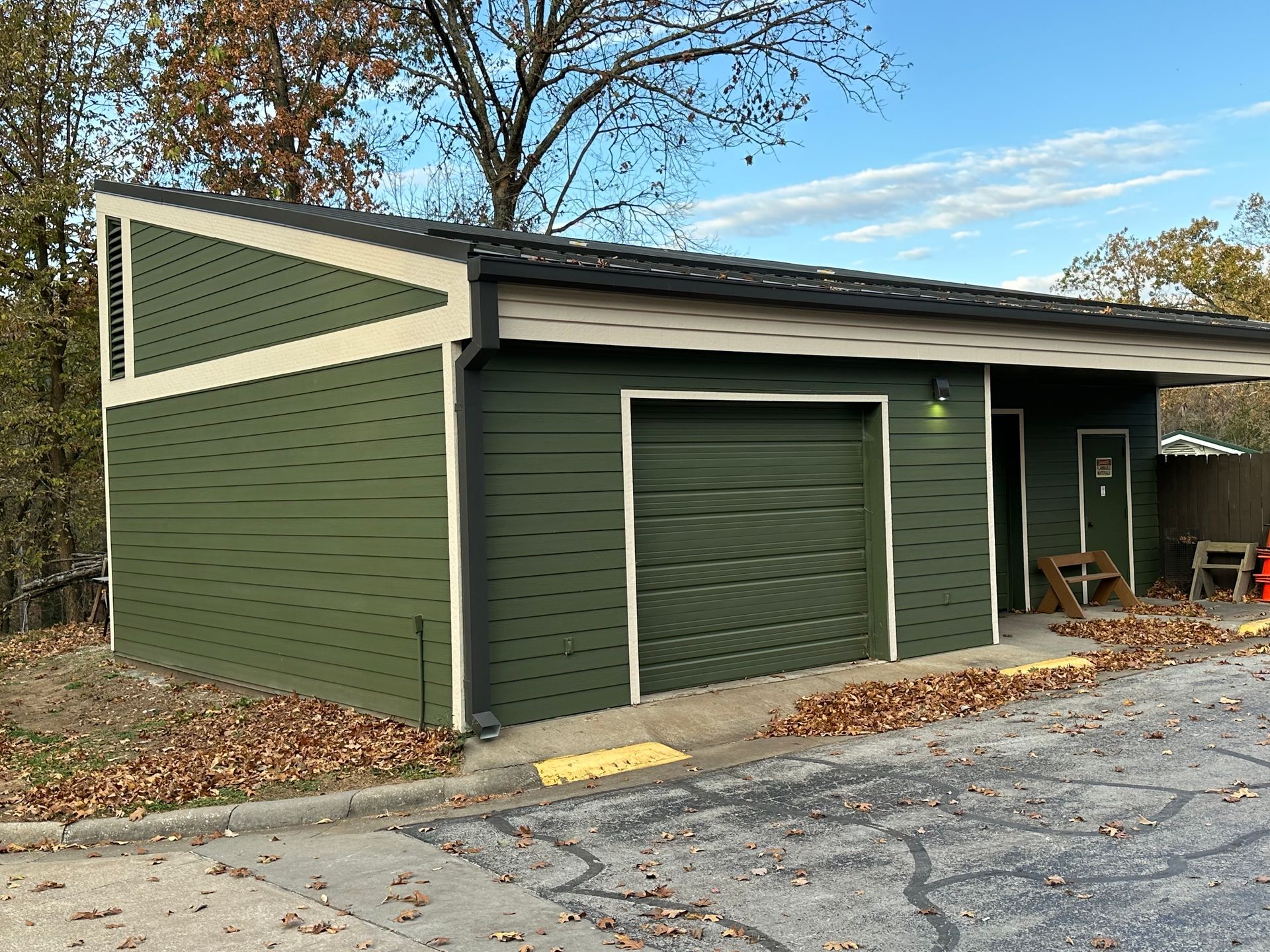 Green building with garage door, angled roof, and small entrance; set on paved area.