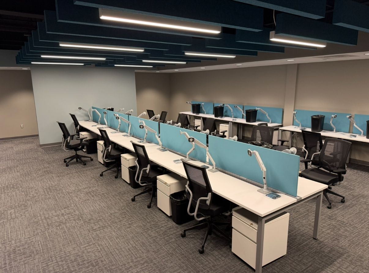 Office workstation with long desks, computers, blue screens, and rolling chairs; neutral color scheme.