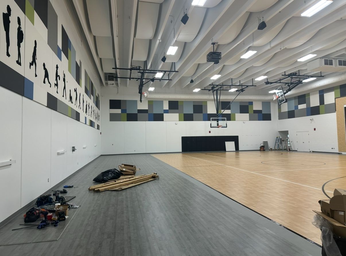 Gym interior with basketball court, colorful wall tiles, and equipment on the floor.