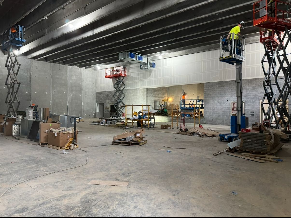 Construction site interior with workers on scissor lifts, concrete walls, and exposed ceiling beams.