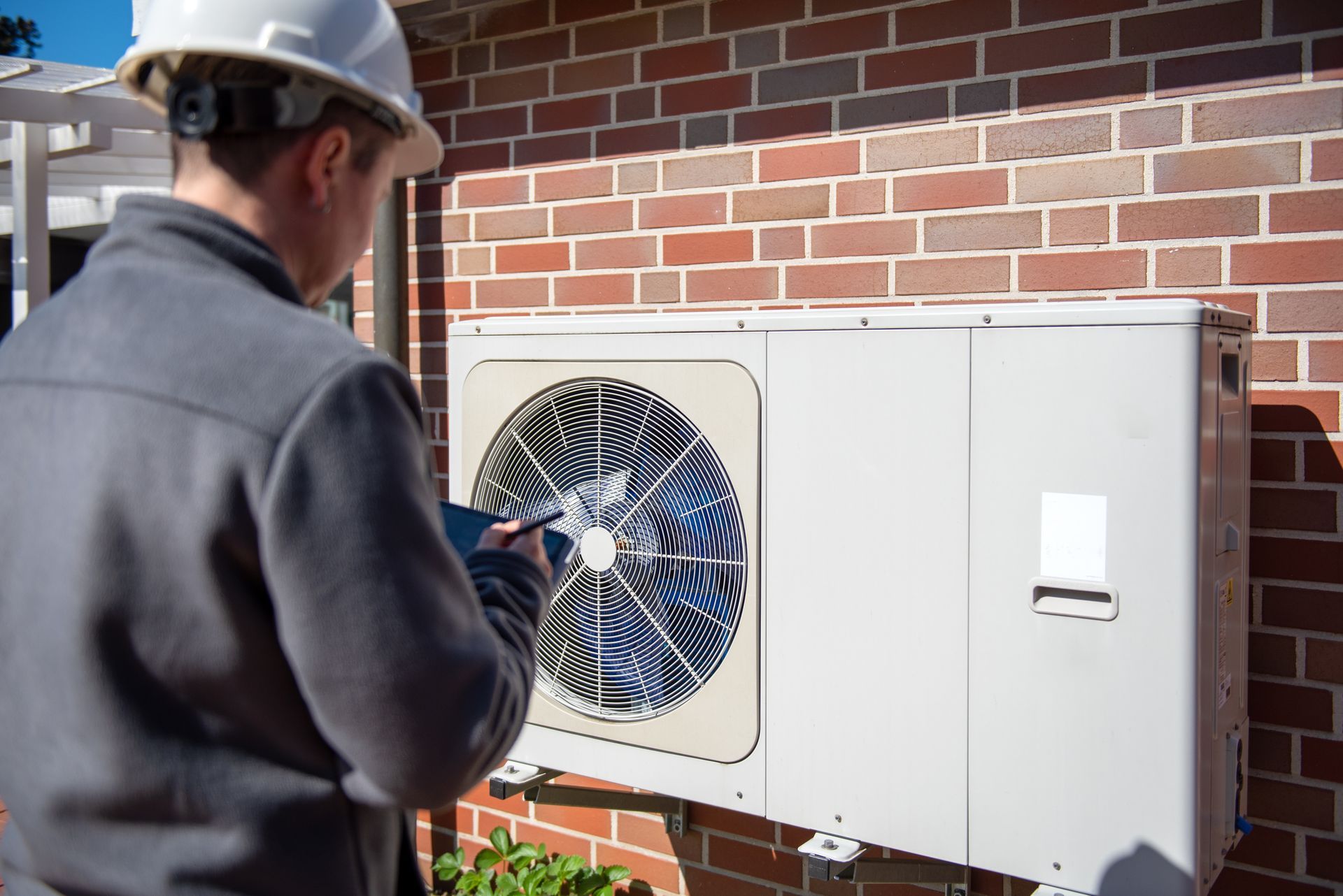 A male technician is inspecting an outdoor residential heating system unit.