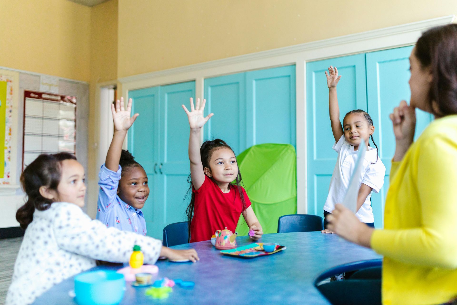 A group of children are raising their hands in a classroom.
