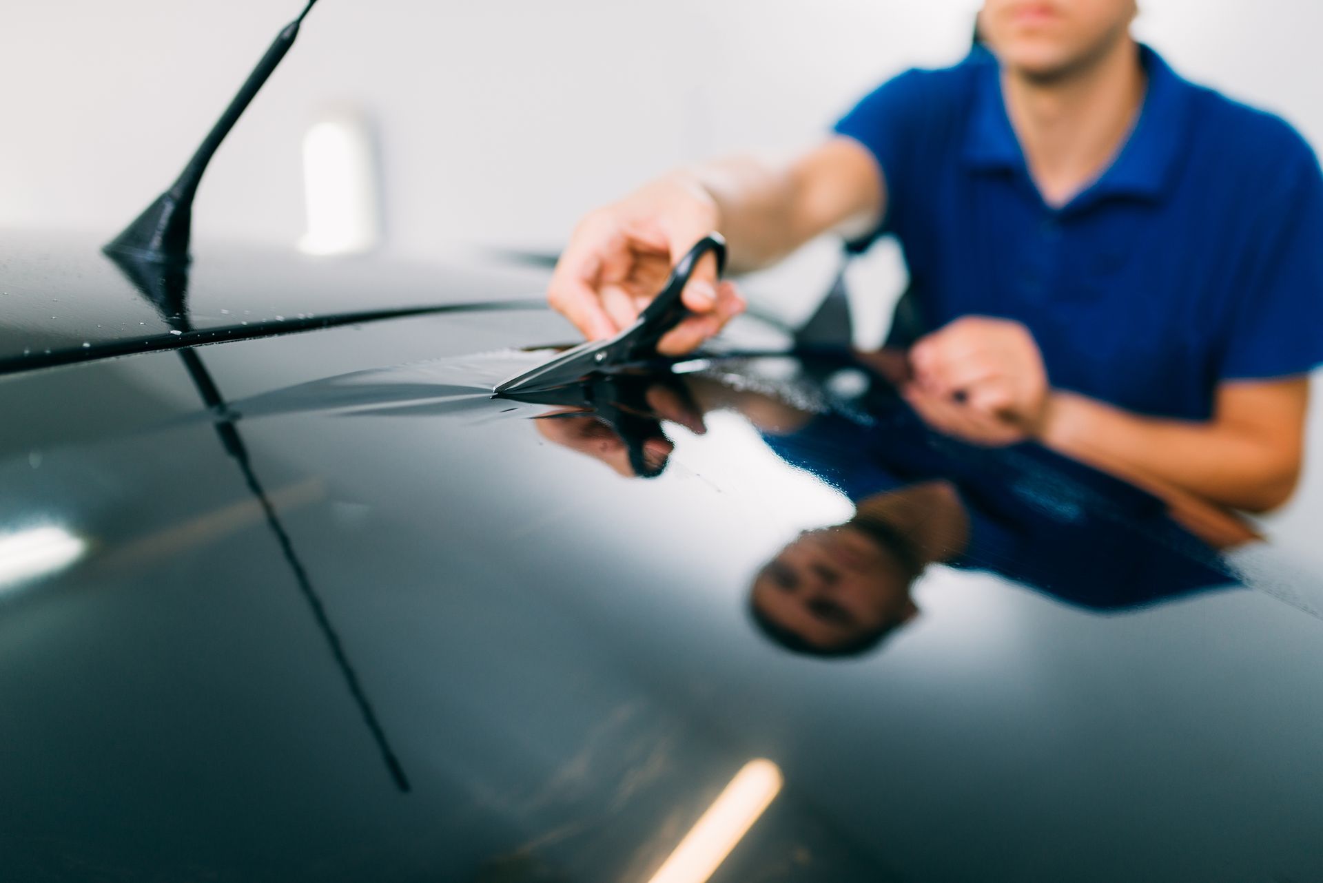 A man is cutting the roof of a car with scissors.