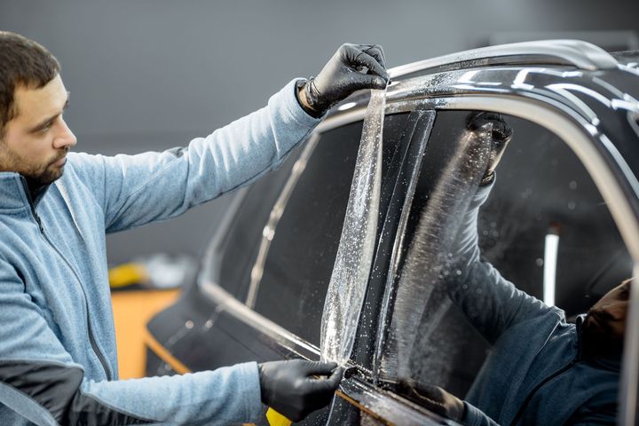 A man is applying tinted glass to a car window.