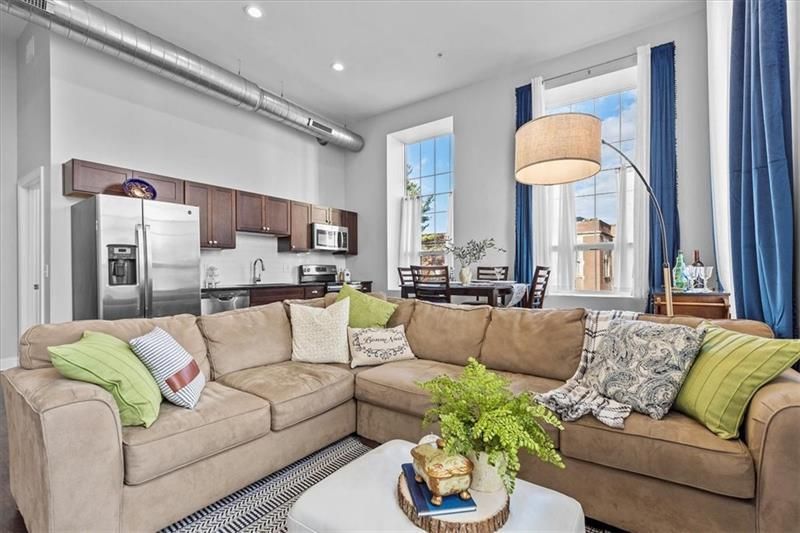 Living room with a tan sectional sofa, kitchen, and large windows with blue curtains.