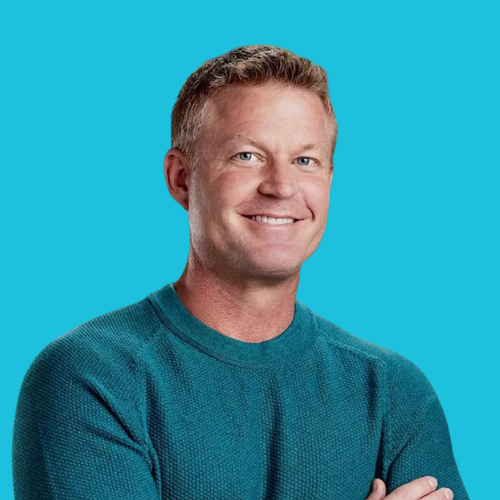 Man smiling, arms crossed, wearing teal sweater against a blue backdrop.
