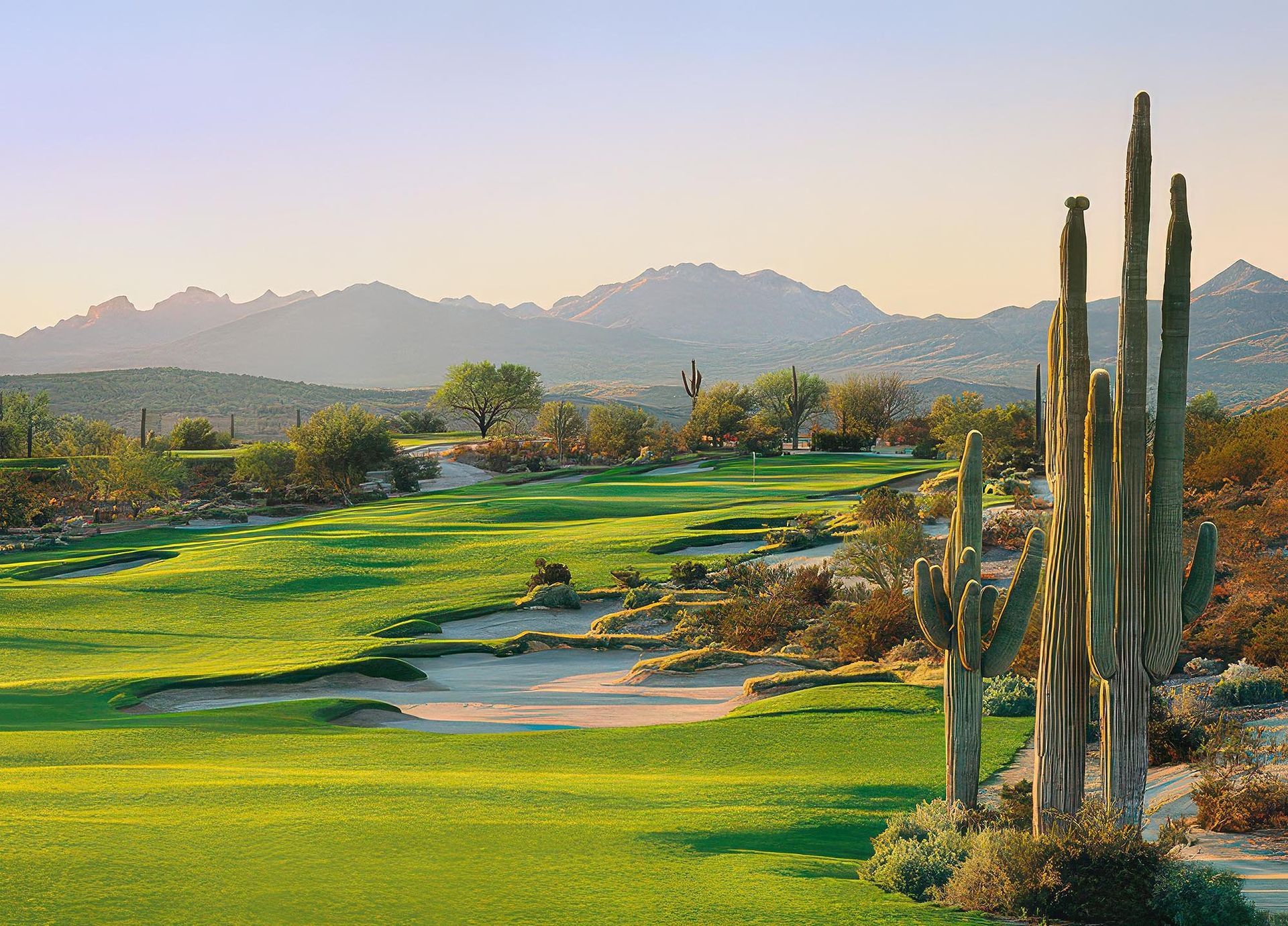 Desert golf course with lush green fairways, sand traps, and tall cacti under a hazy mountain backdrop