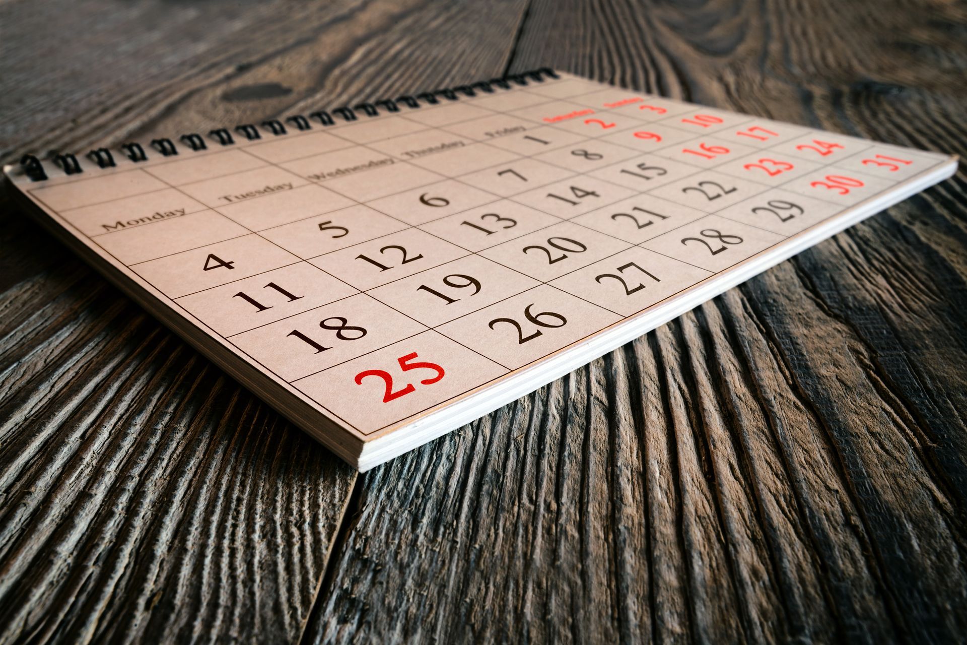 Desk calendar on a wooden table, showing dates in black and red numbers.