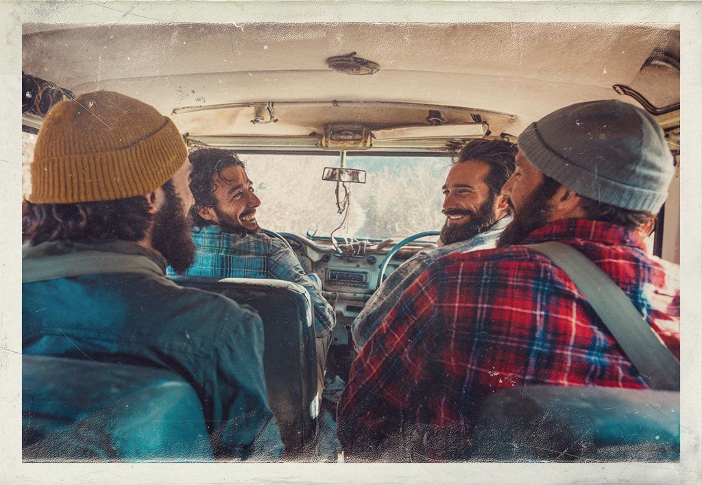 Four friends chat inside a van, seen from the back seats, with knit hats and a red plaid shirt.