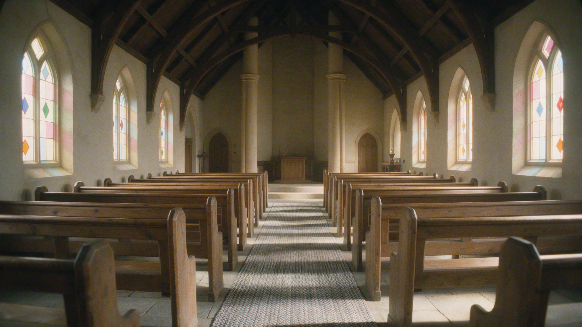 Empty church sanctuary with wooden pews and stained glass windows on both sides.