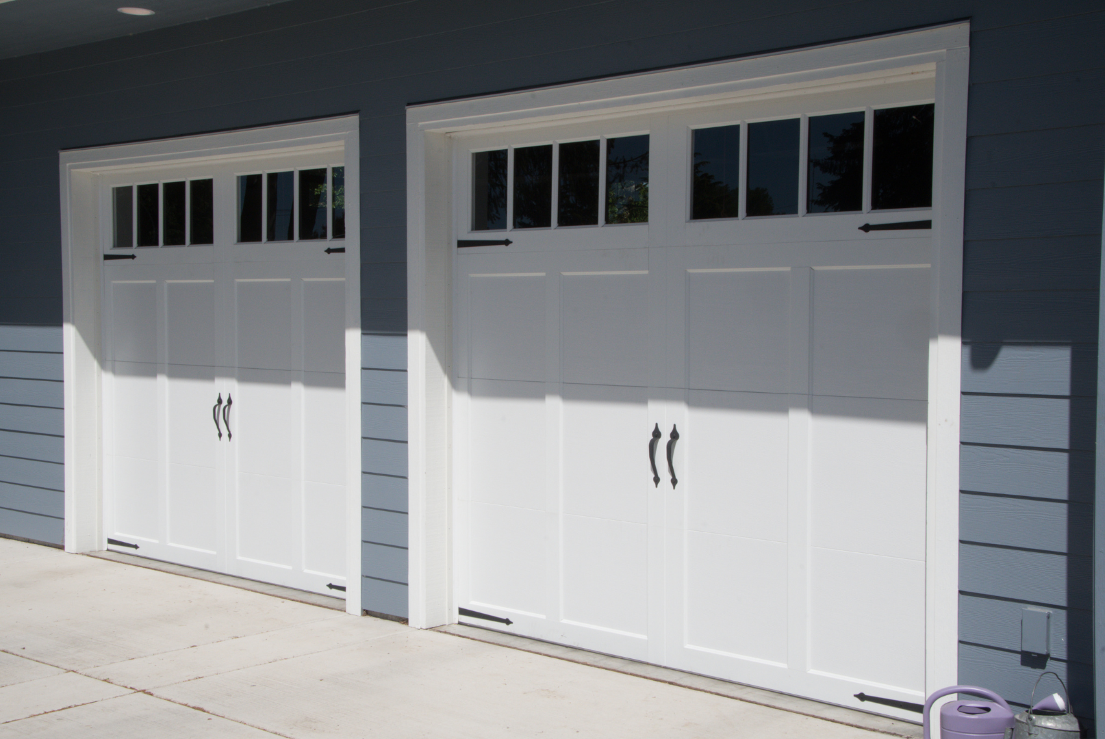 Two wooden garage doors with window panes at the top. The doors are brown and have vertical paneling.