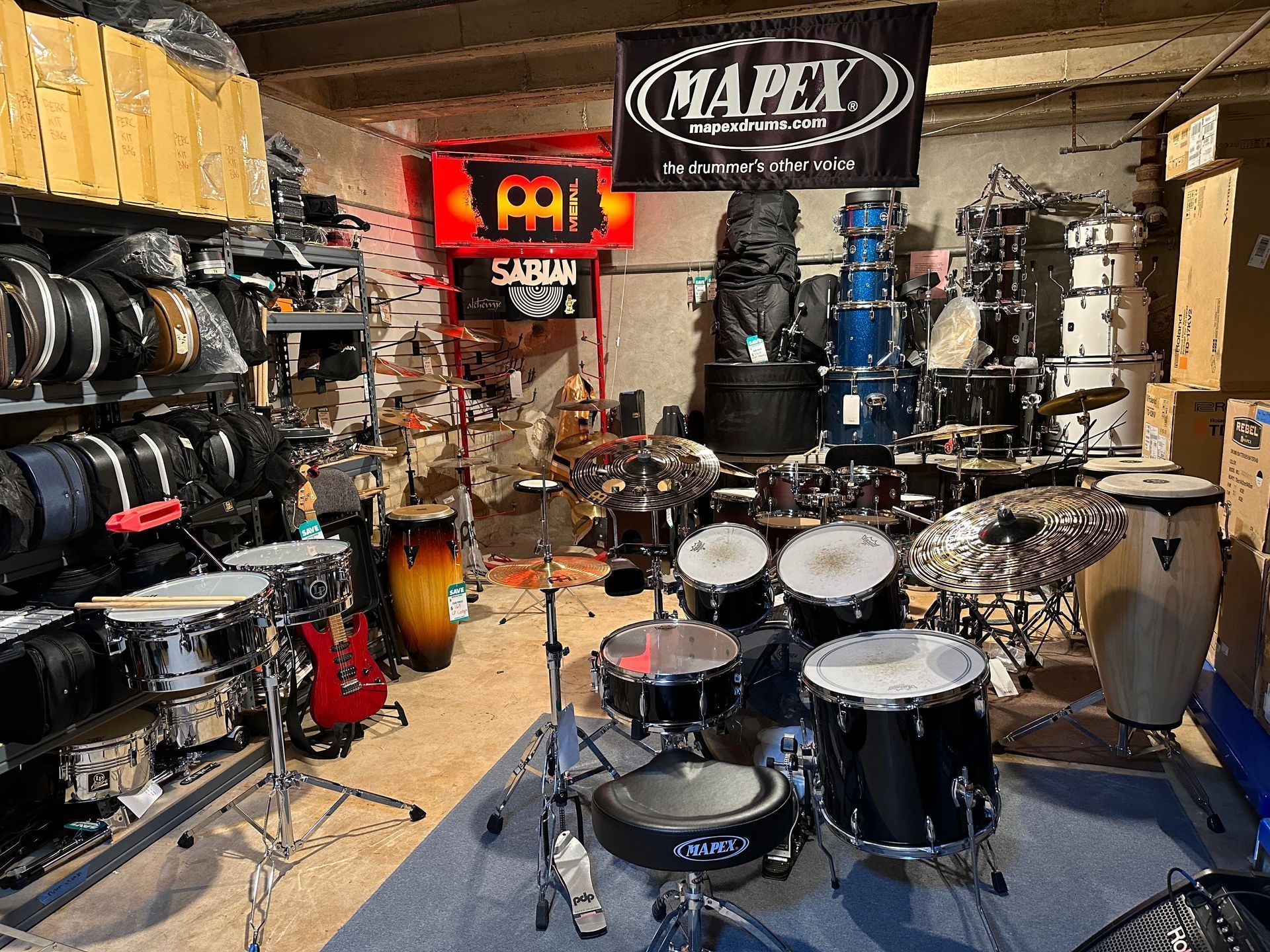 Drum set storage room, many drums and cymbals visible. Some are assembled, others are stored with related equipment.