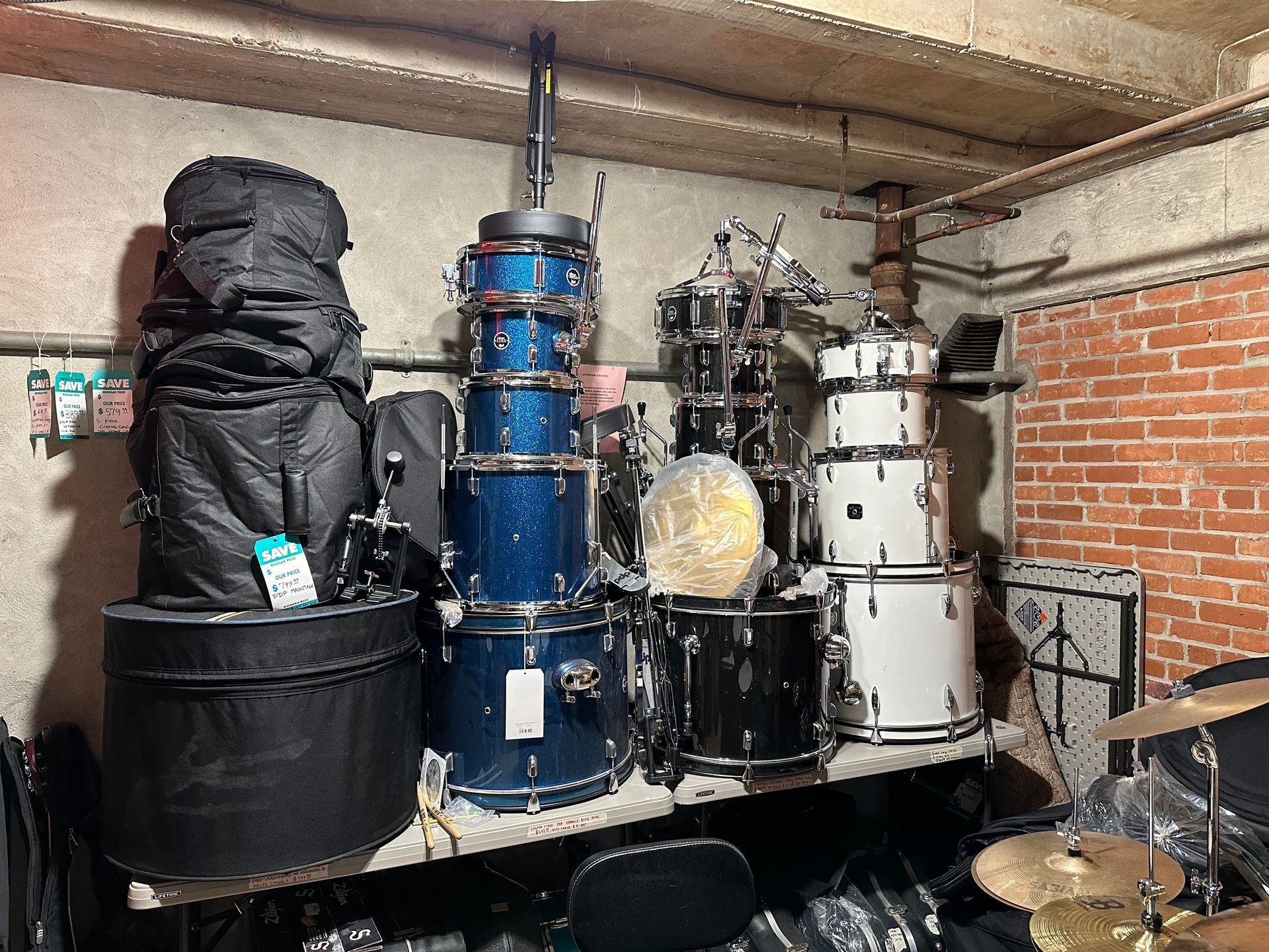 A collection of drum sets and cases stored in a room with brick walls.