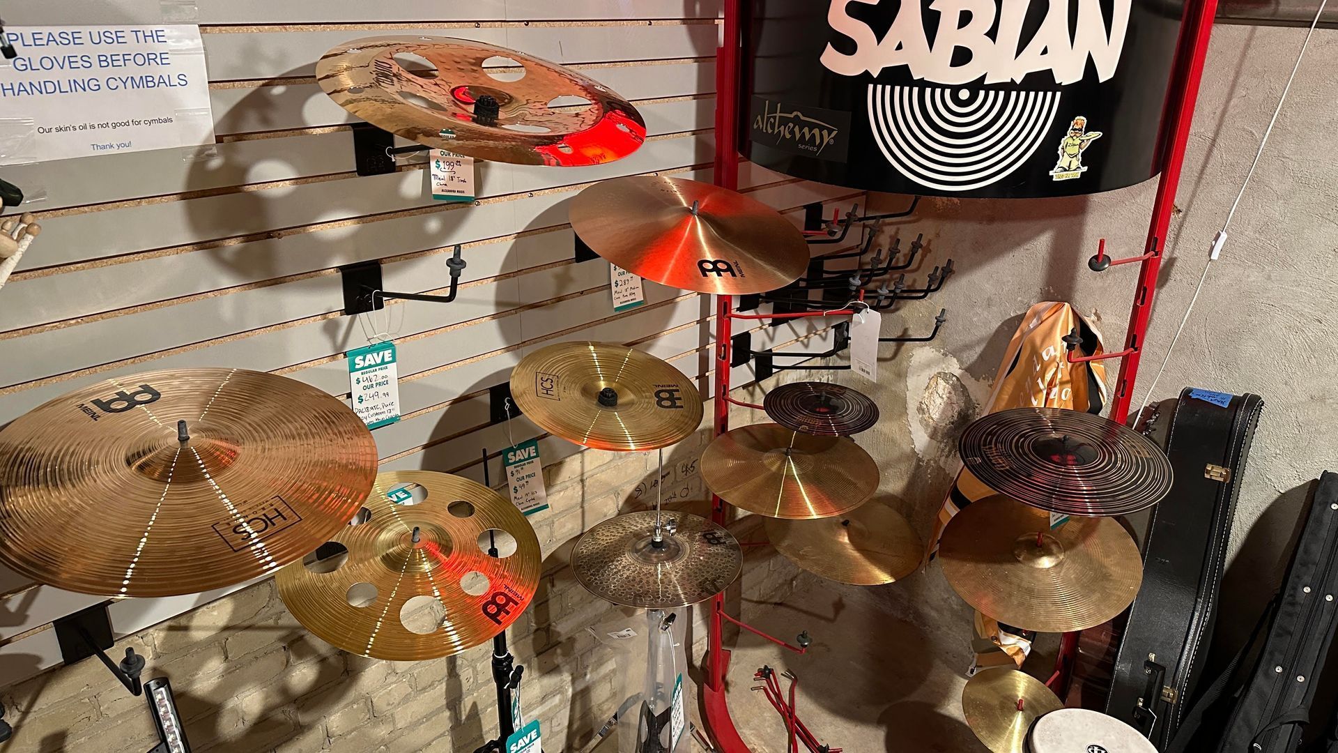Cymbals of various sizes and colors displayed on a wall in a music store, with a Sabian drum case.