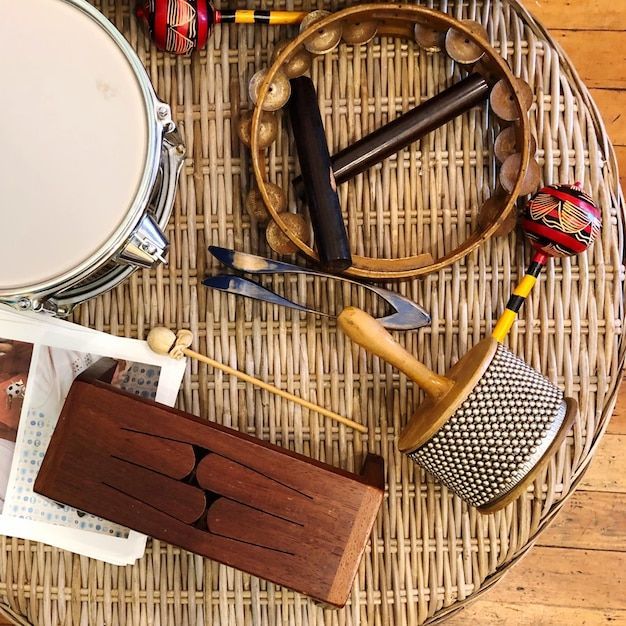 Overhead shot of various percussion instruments on a woven table: drum, tambourine, maracas, wood drum, and scrapers.