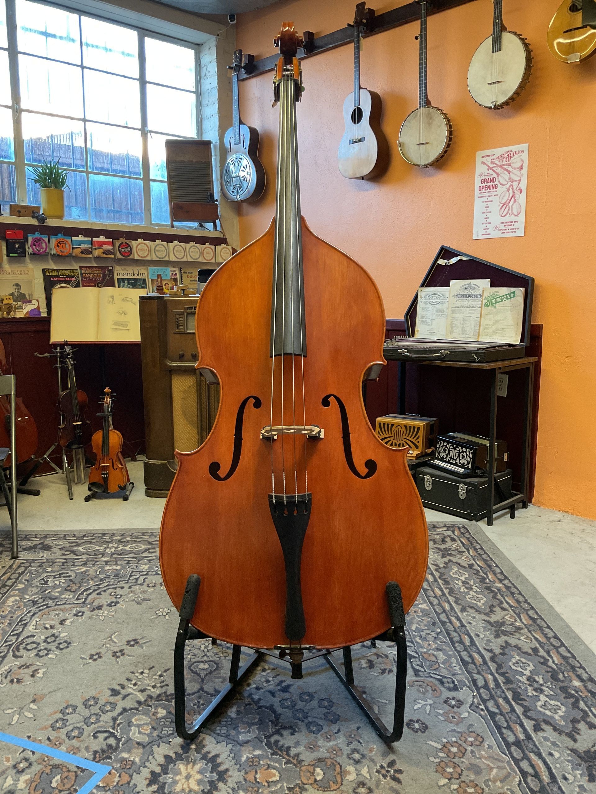 Upright bass on a black stand in a music shop, with other instruments on the wall.