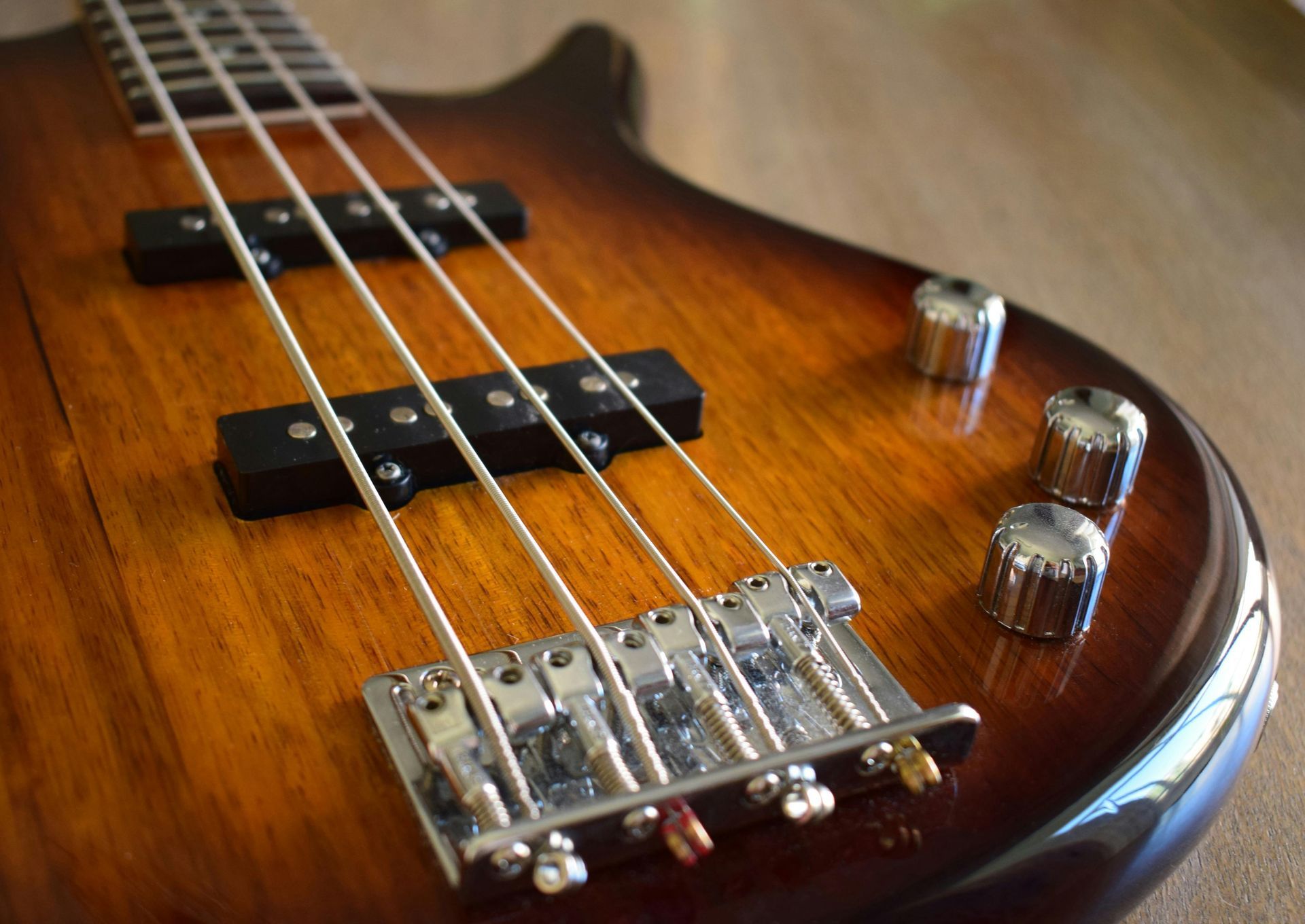 Close-up of a brown and amber bass guitar, showcasing strings, pickups, and bridge.