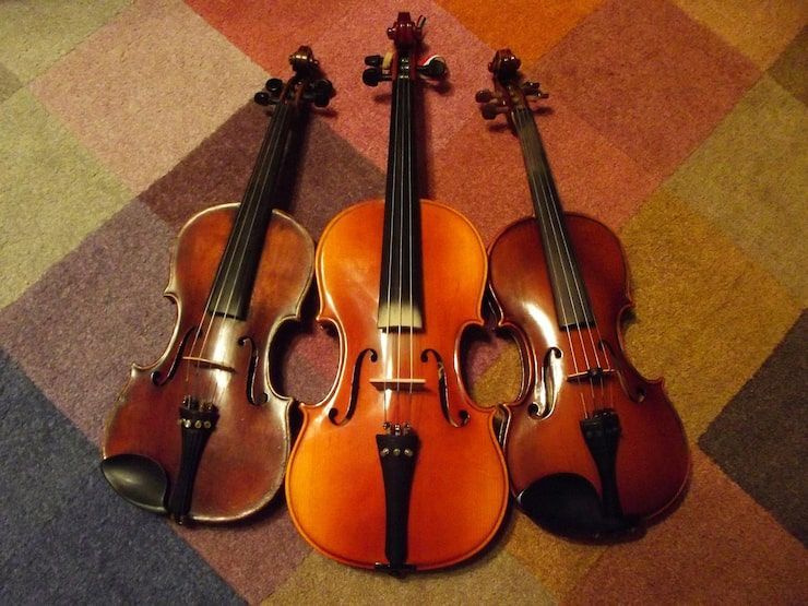 Three string instruments: two violins and a cello, arranged on a patterned rug.
