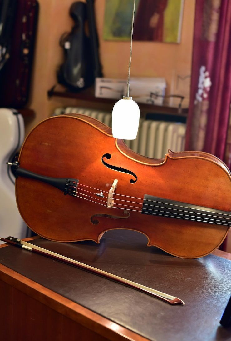 Cello with bow on a brown surface, a light fixture above, and a muted background.