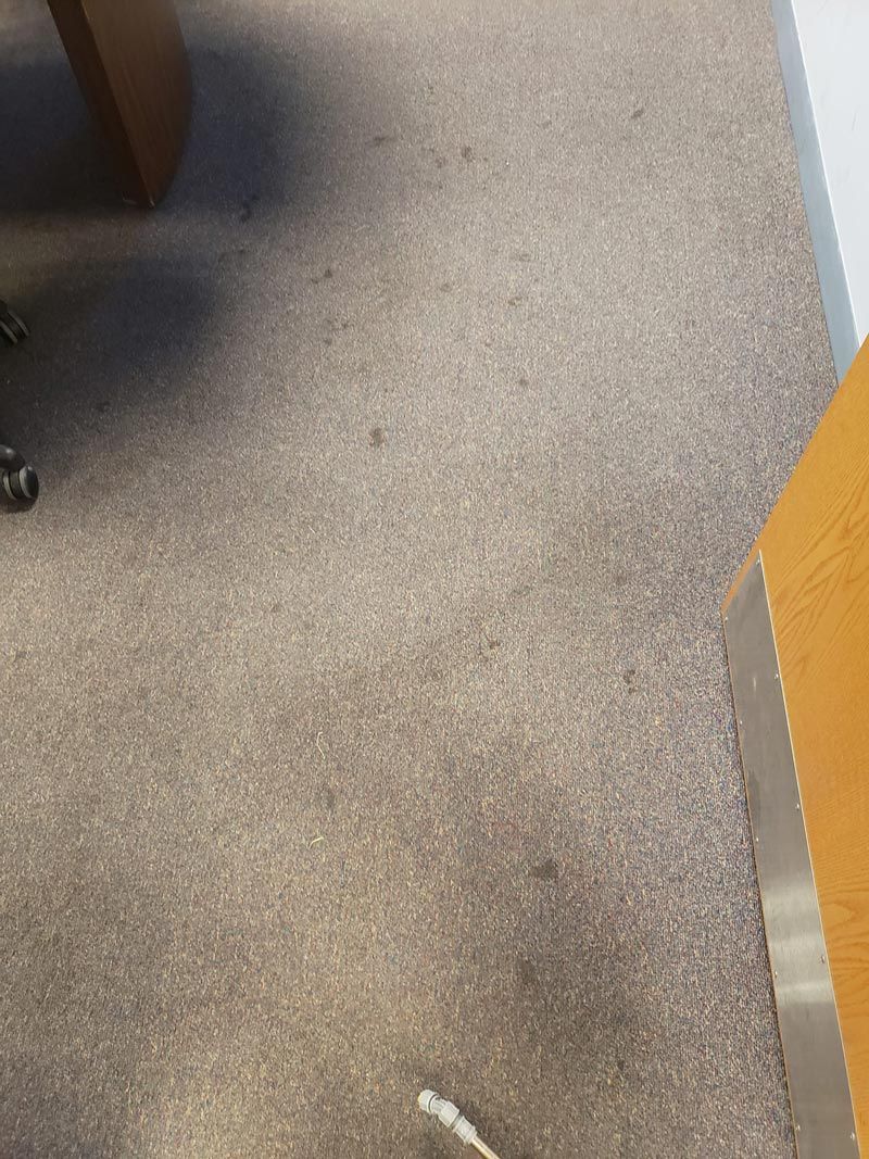 A close up of a carpeted floor in an office with a desk and chair.