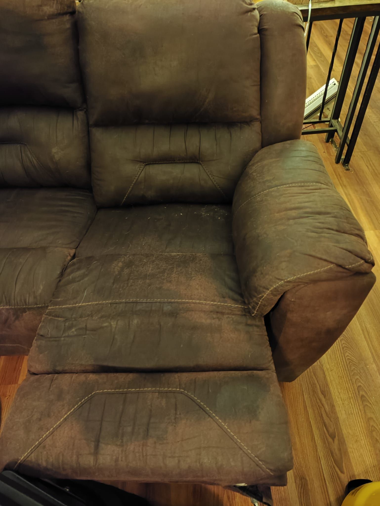 A brown leather recliner couch is sitting on a wooden floor.