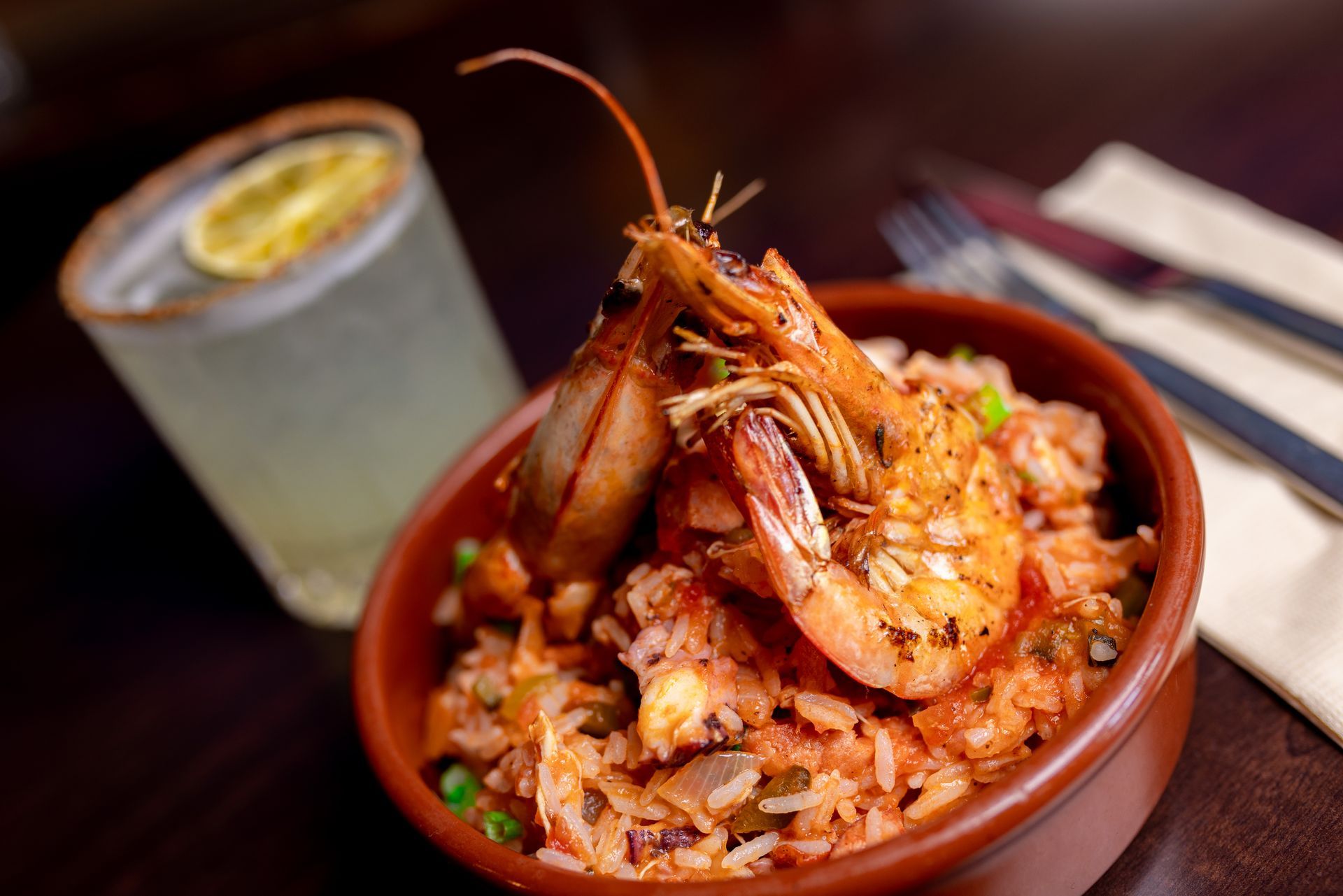A bowl of shrimp and rice next to a drink on a table.