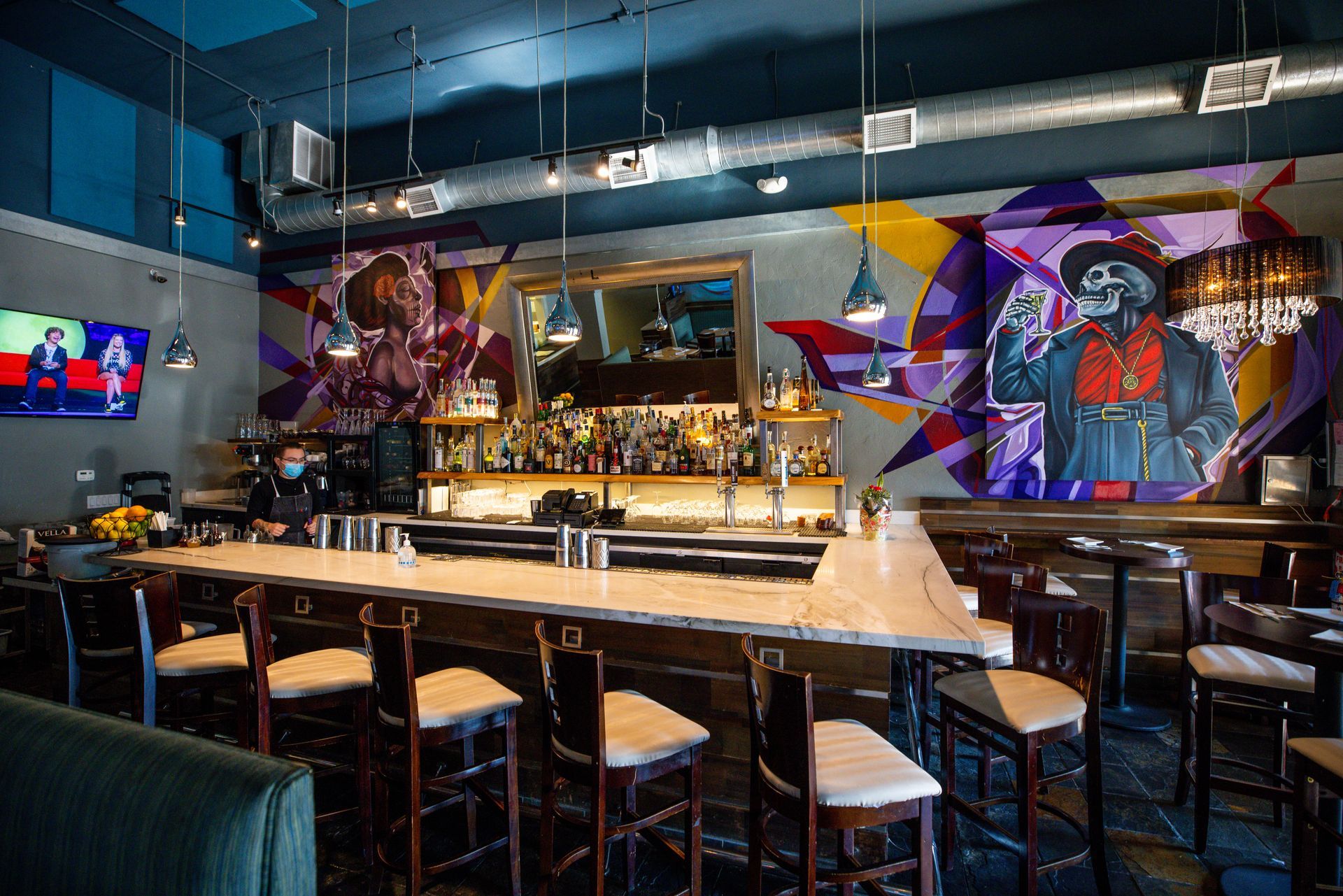 A restaurant with a long bar and a mural on the wall.