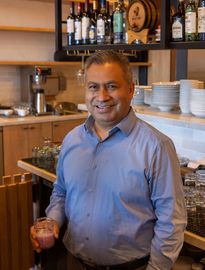 A man in a blue shirt is standing in a kitchen holding a drink.