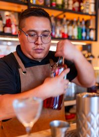 A bartender is pouring a drink into a martini glass.