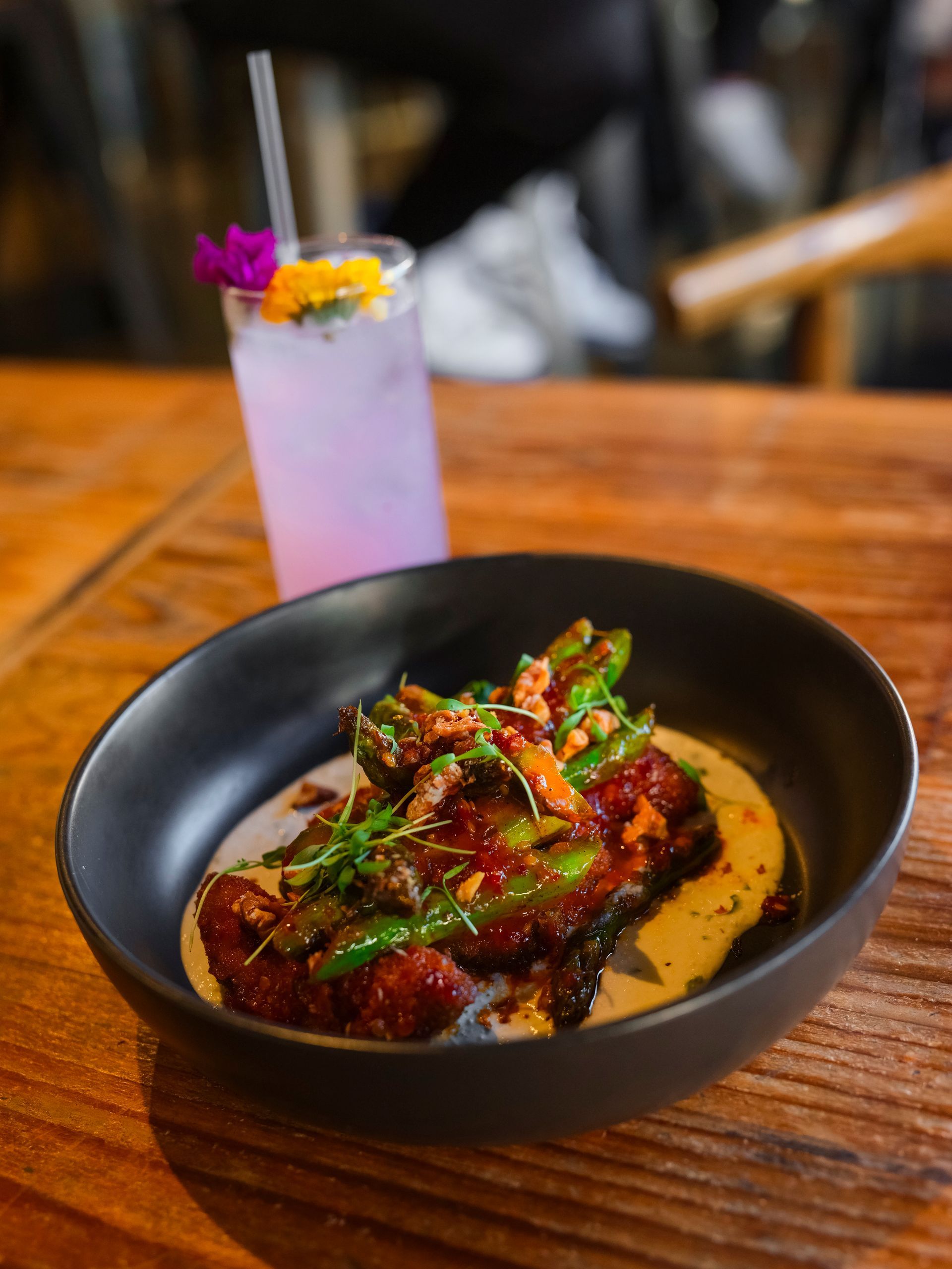 A bowl of food is sitting on a wooden table next to a drink.