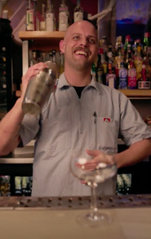 A bartender is smiling while pouring a drink into a glass
