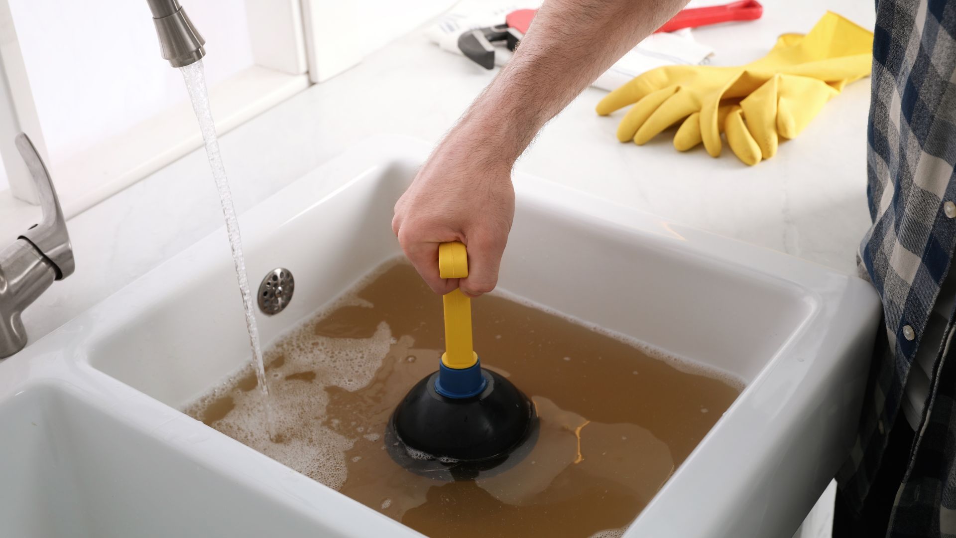 Person plunging a clogged kitchen sink filled with dirty brown water.
